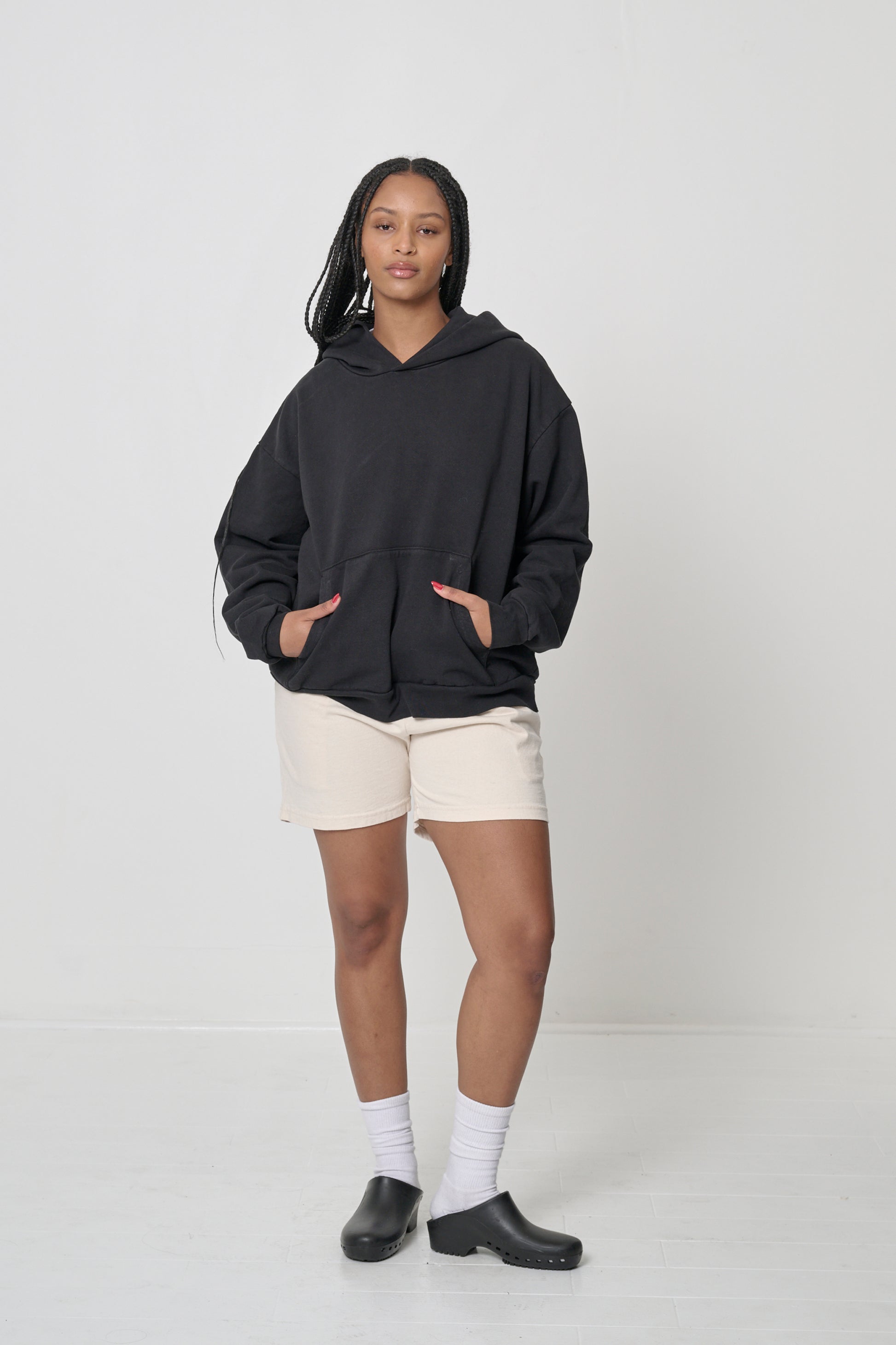 Front full length: woman wearing a Black Trash Hoodie with hands in the kangaroo pocket