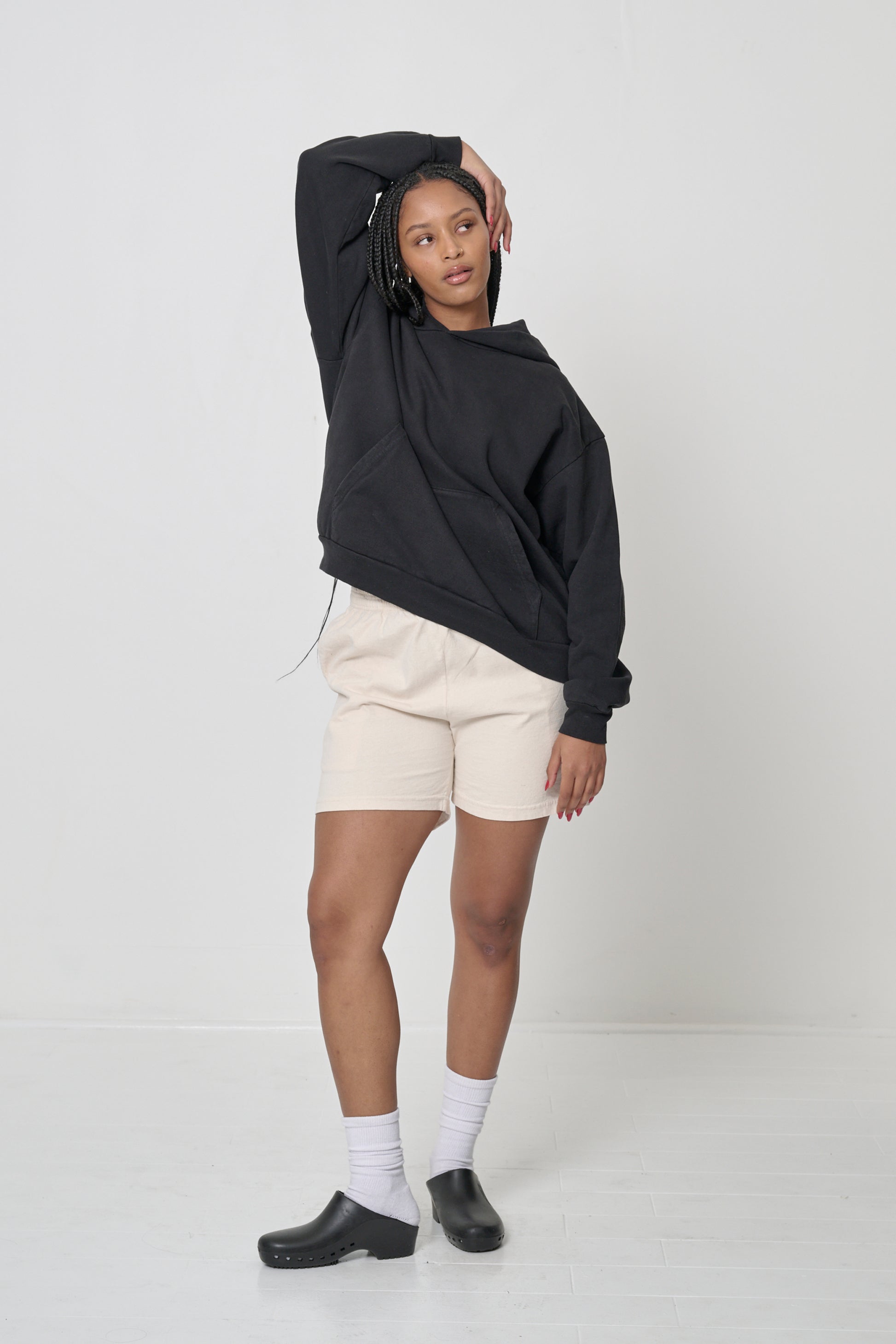 Front view: woman in a Black Trash Hoodie with one arm over her head, showing easy and comfortable movement.