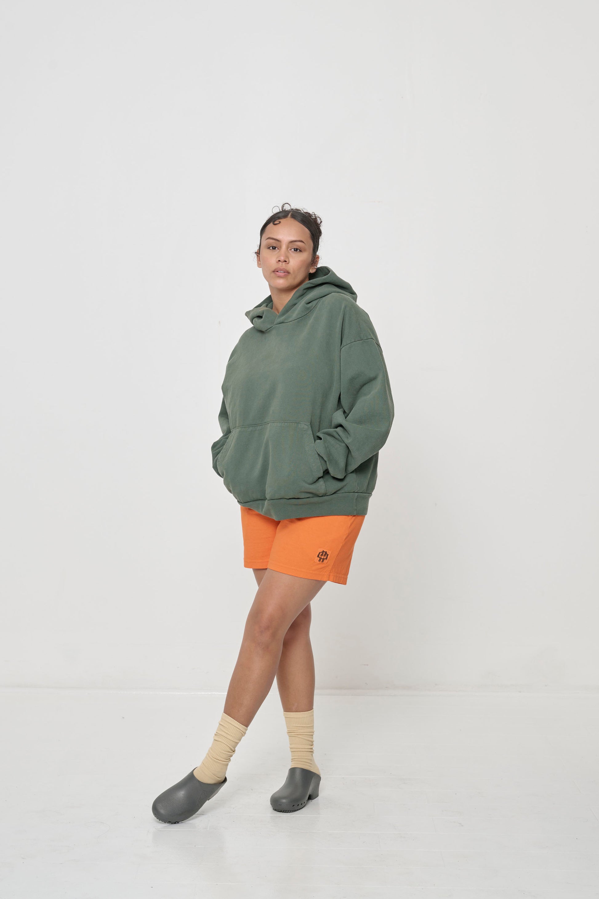 3/4 front full length: woman wearing a Pine Trash Hoodie with hands in the kangaroo pocket