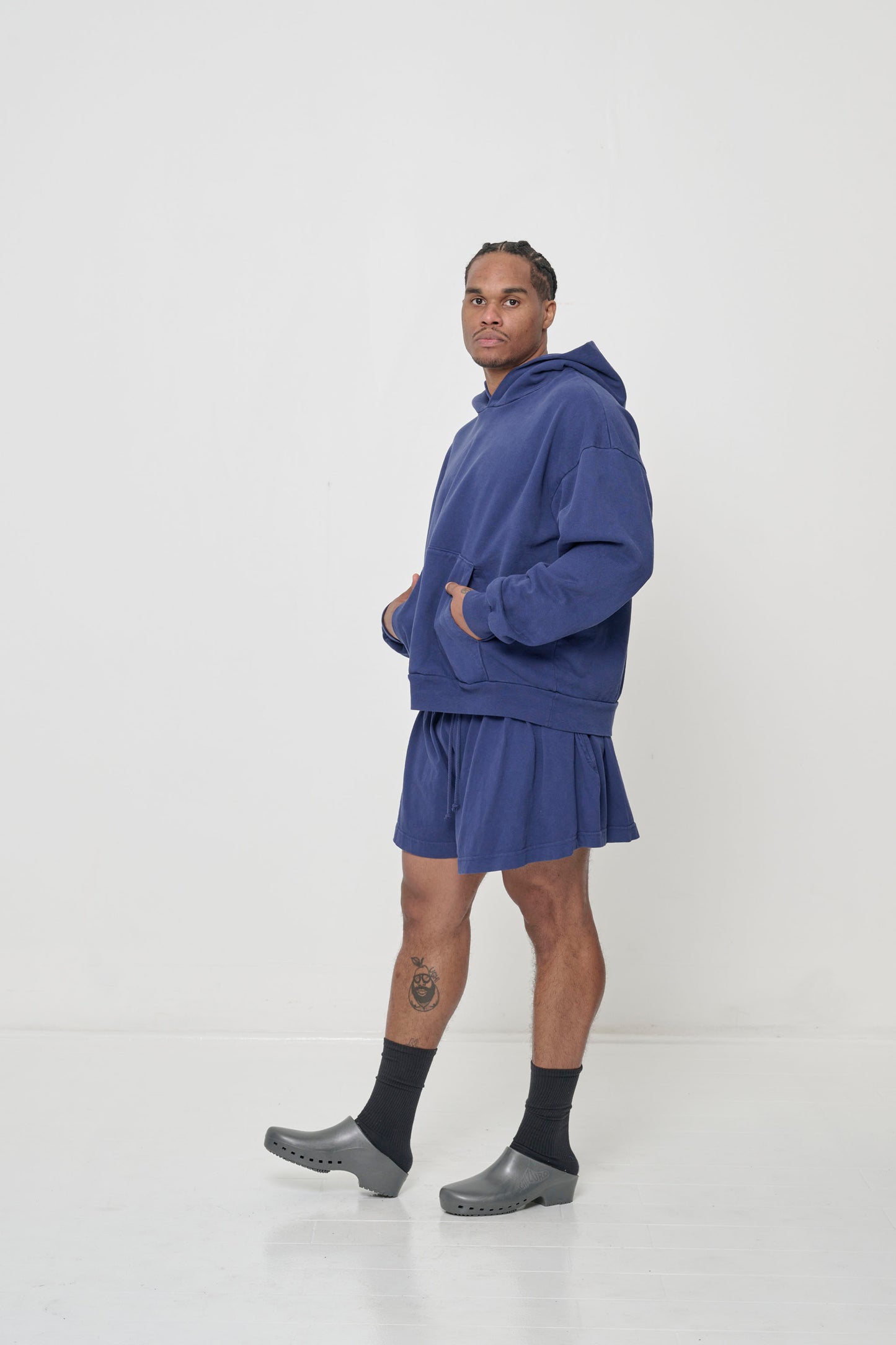 Profile full length view: man wearing a Washed Navy Trash Hoodie with hands in the kangaroo pocket.