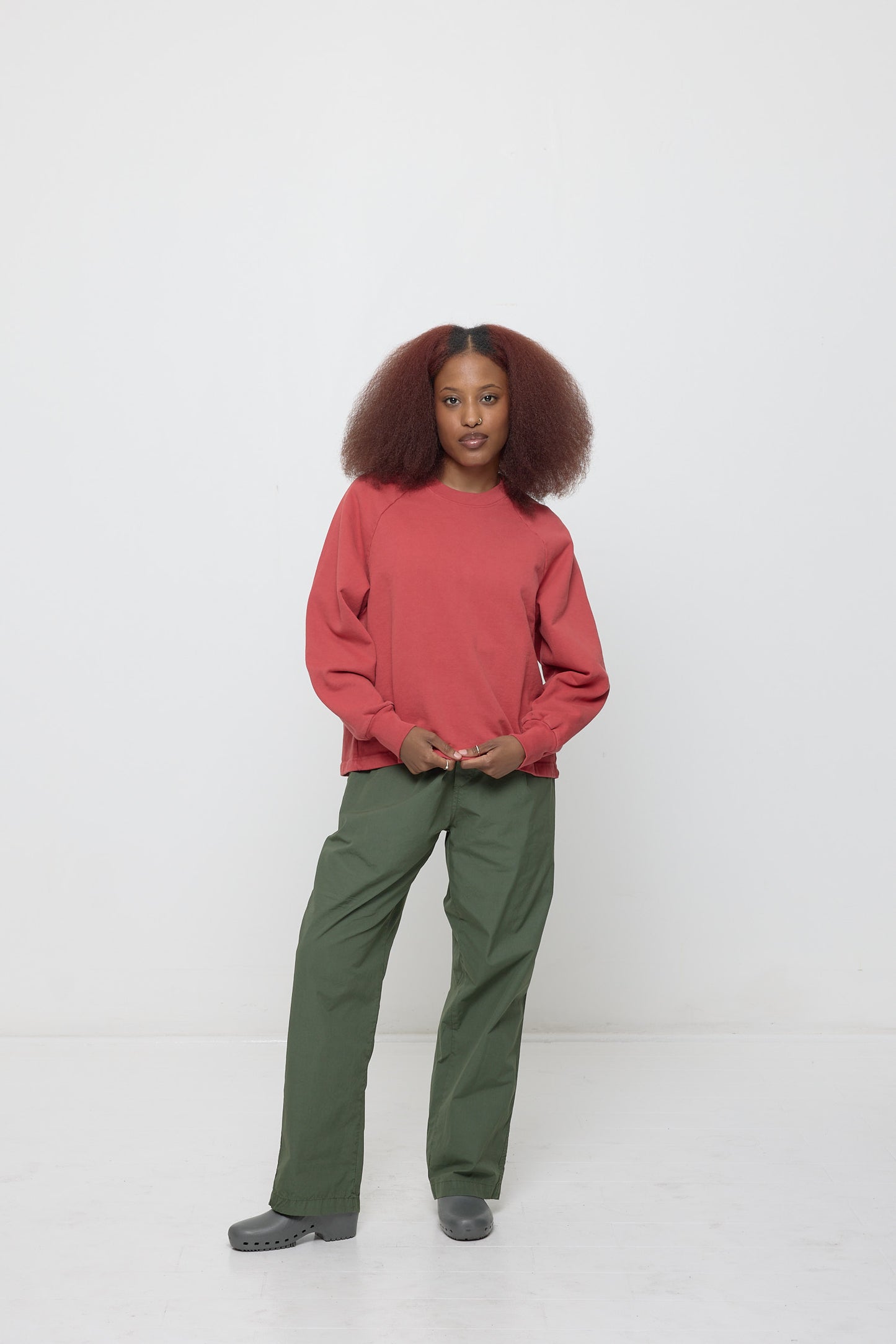 Front full length: woman in a Cedar Trash Raglan, lightly pulling on hem to show soft fabric folds of the cotton fleece.