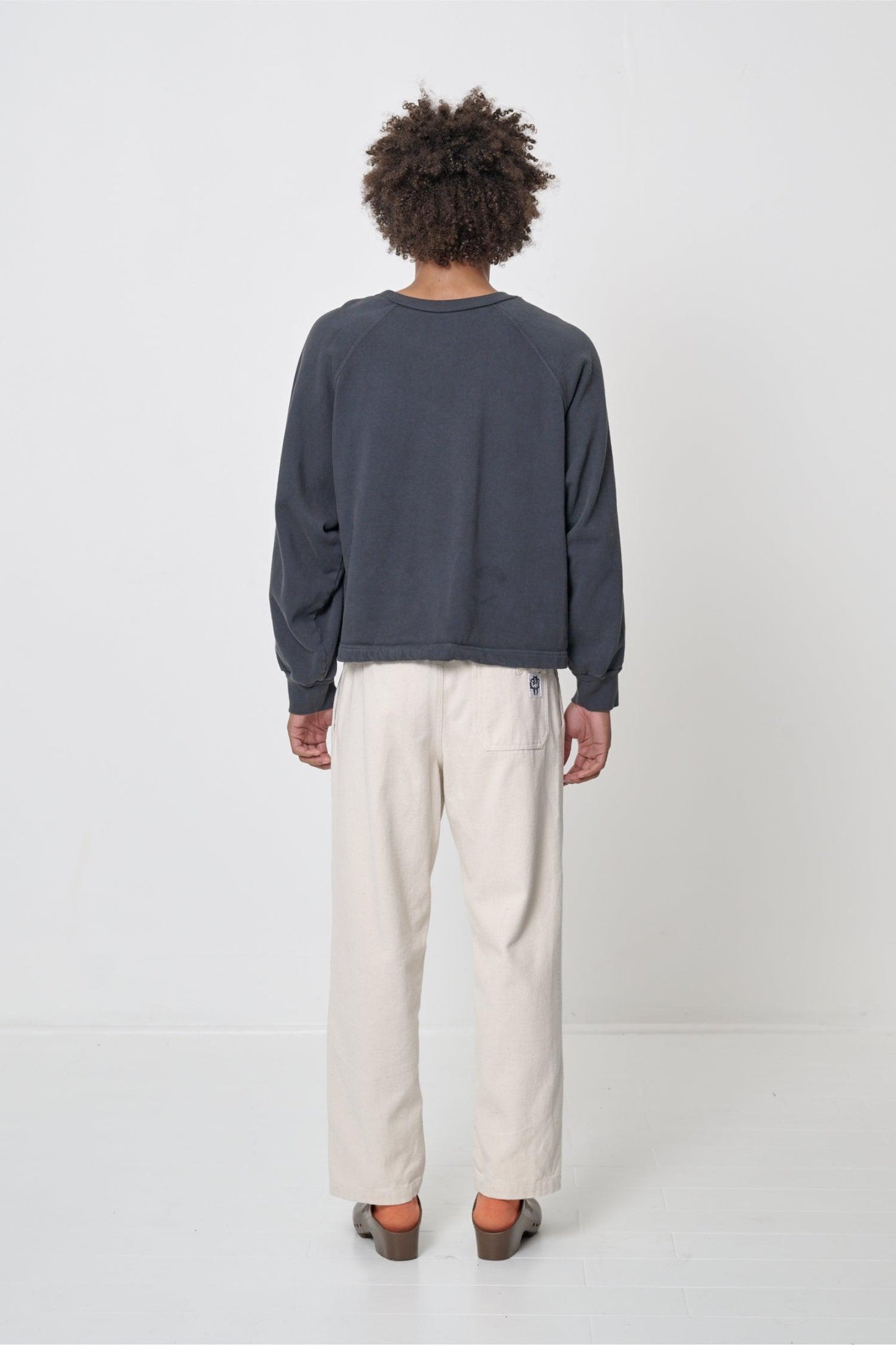 Slate Trash Crewneck, back view on a person. Relaxed throughout except for the rib cuffs.