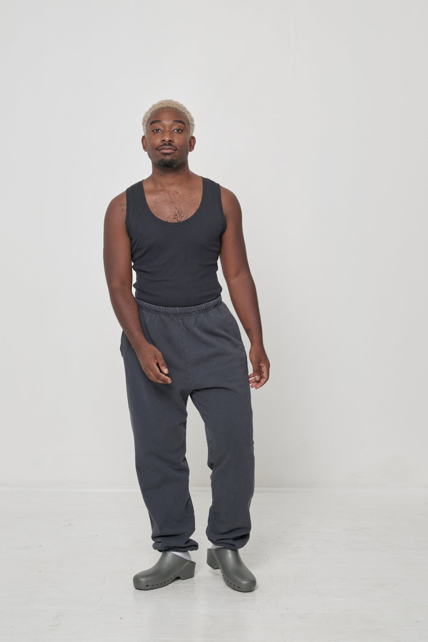A man in matching Slate The Tank and Trash Sweatpants. One knee popped to show inseam and pant leg width.