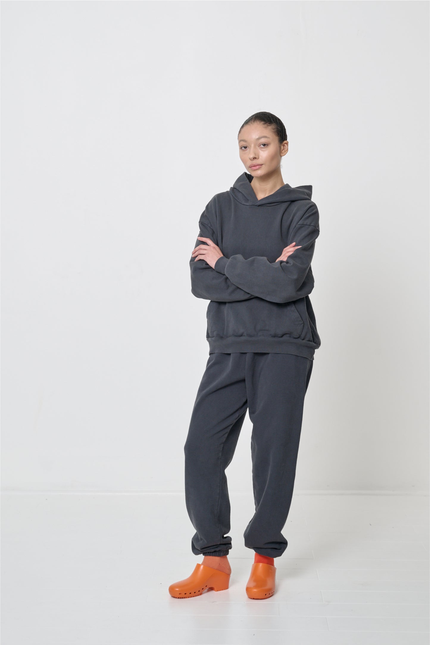 Woman in matching Slate Trash Hoodie and Trash Sweatpants, arms crossed. A knee popped shows inseam and pant leg width.