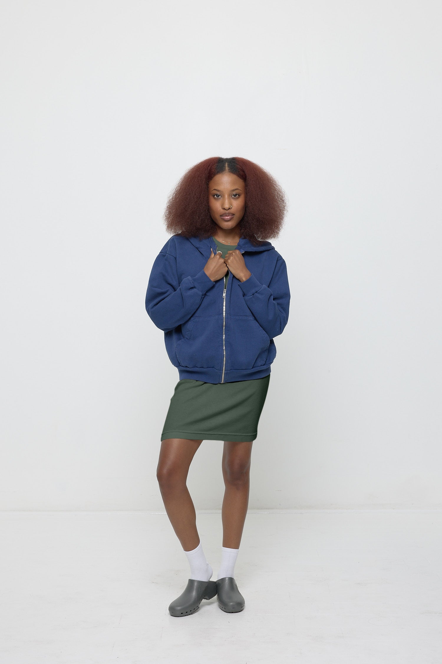 Front view: woman wearing partially zipped Washed Navy Trash Zip Up Hoodie with hands just below the collar.