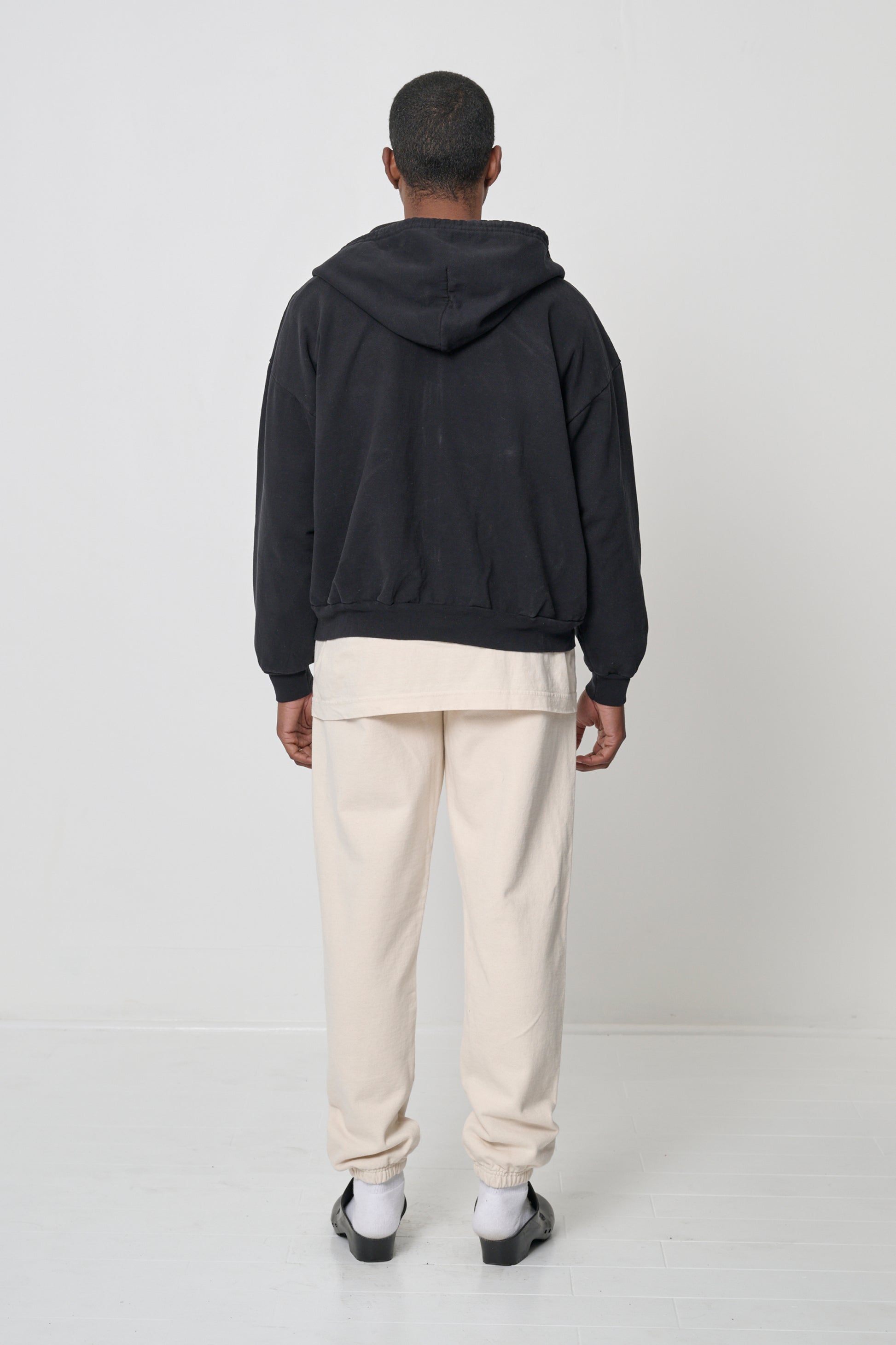 Back view: Man wearing a Black Trash Zip Up Hoodie, highlighting the hood.