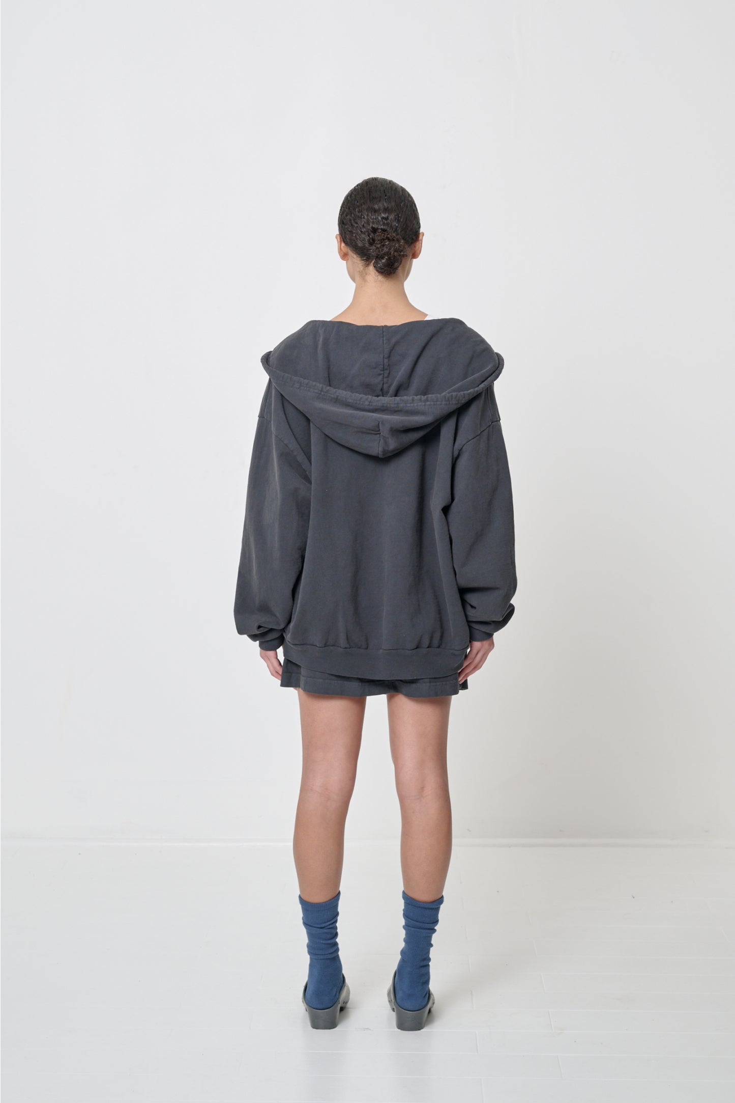 Back view: Woman wearing an unzipped Slate Trash Zip Up Hoodie, such that the hood rests across her shoulders and back.