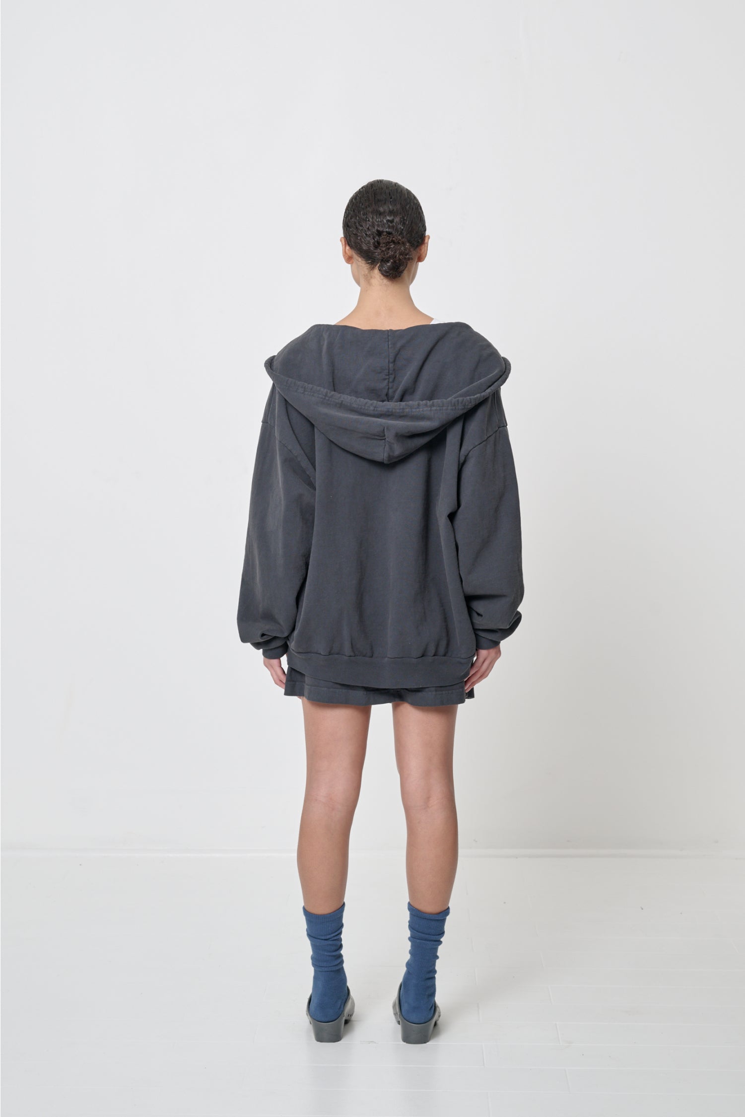 Back view: Woman wearing an unzipped Slate Trash Zip Up Hoodie, such that the hood rests across her shoulders and back.