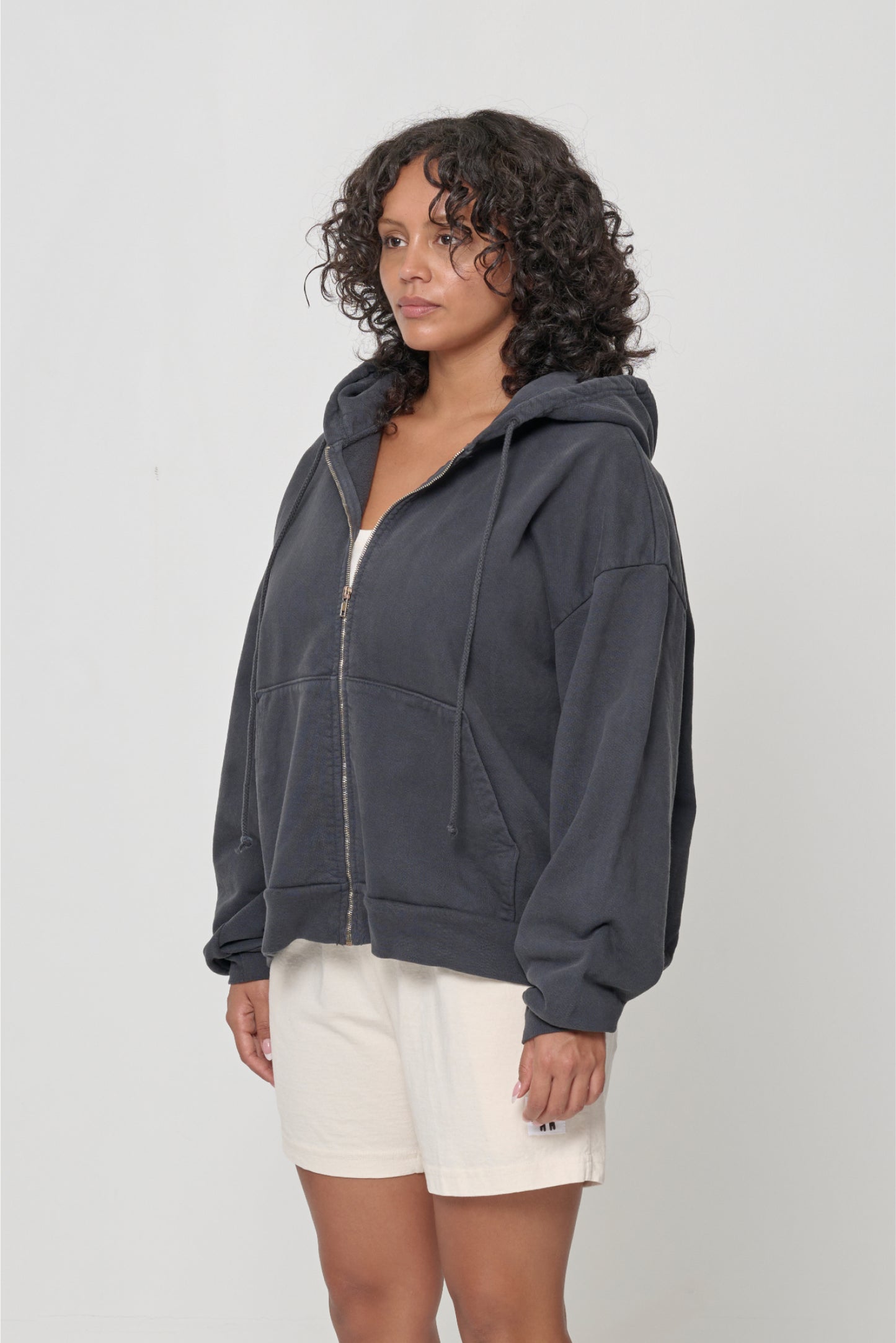 Woman facing 45-degrees, wearing a Slate Trash Zip Up Hoodie, showcasing sleeve's relaxed fit and drop shoulder.