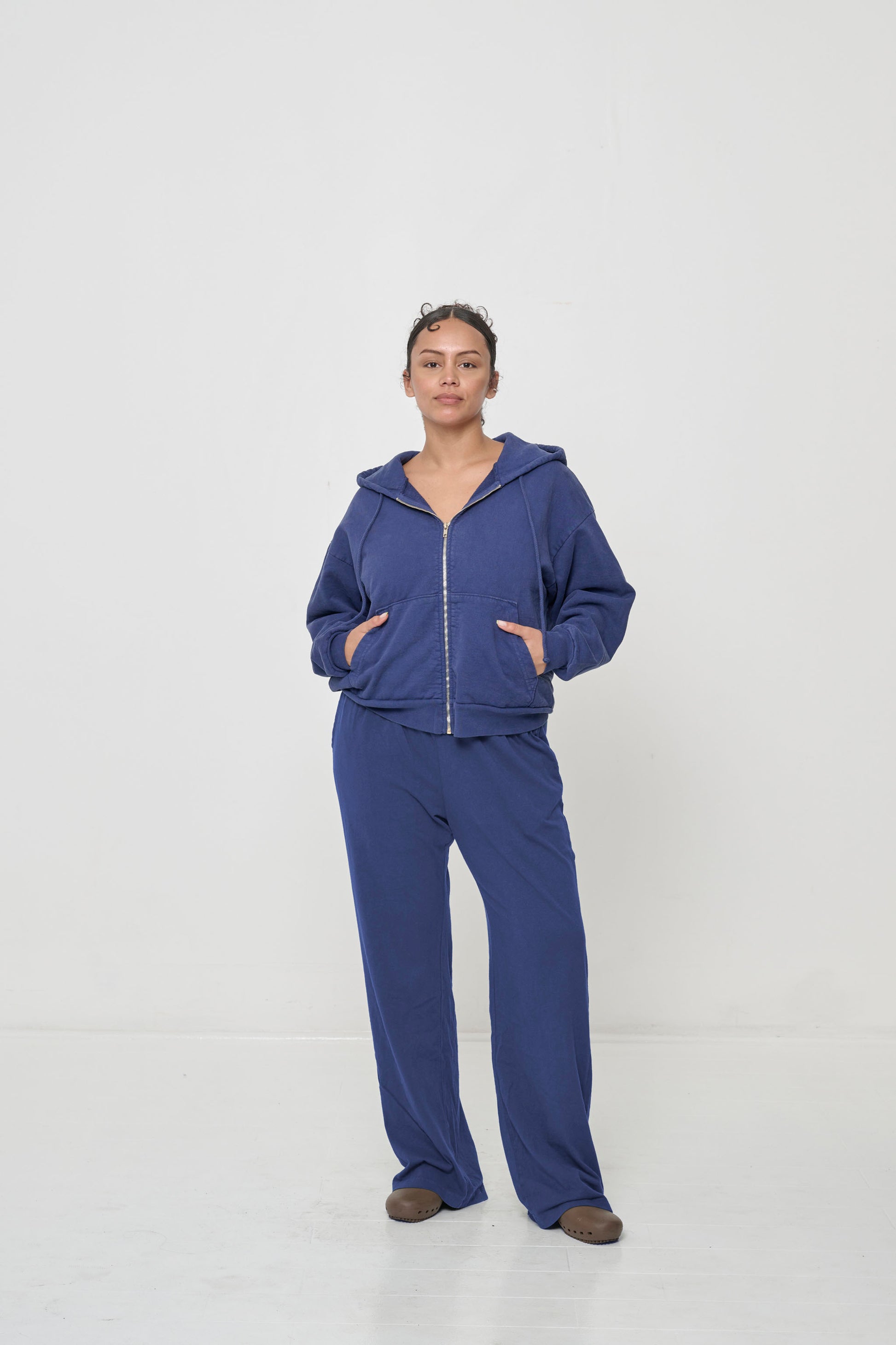 Front view: woman wearing a Washed Navy Trash Zip Up Hoodie with hands in the kangaroo pockets.