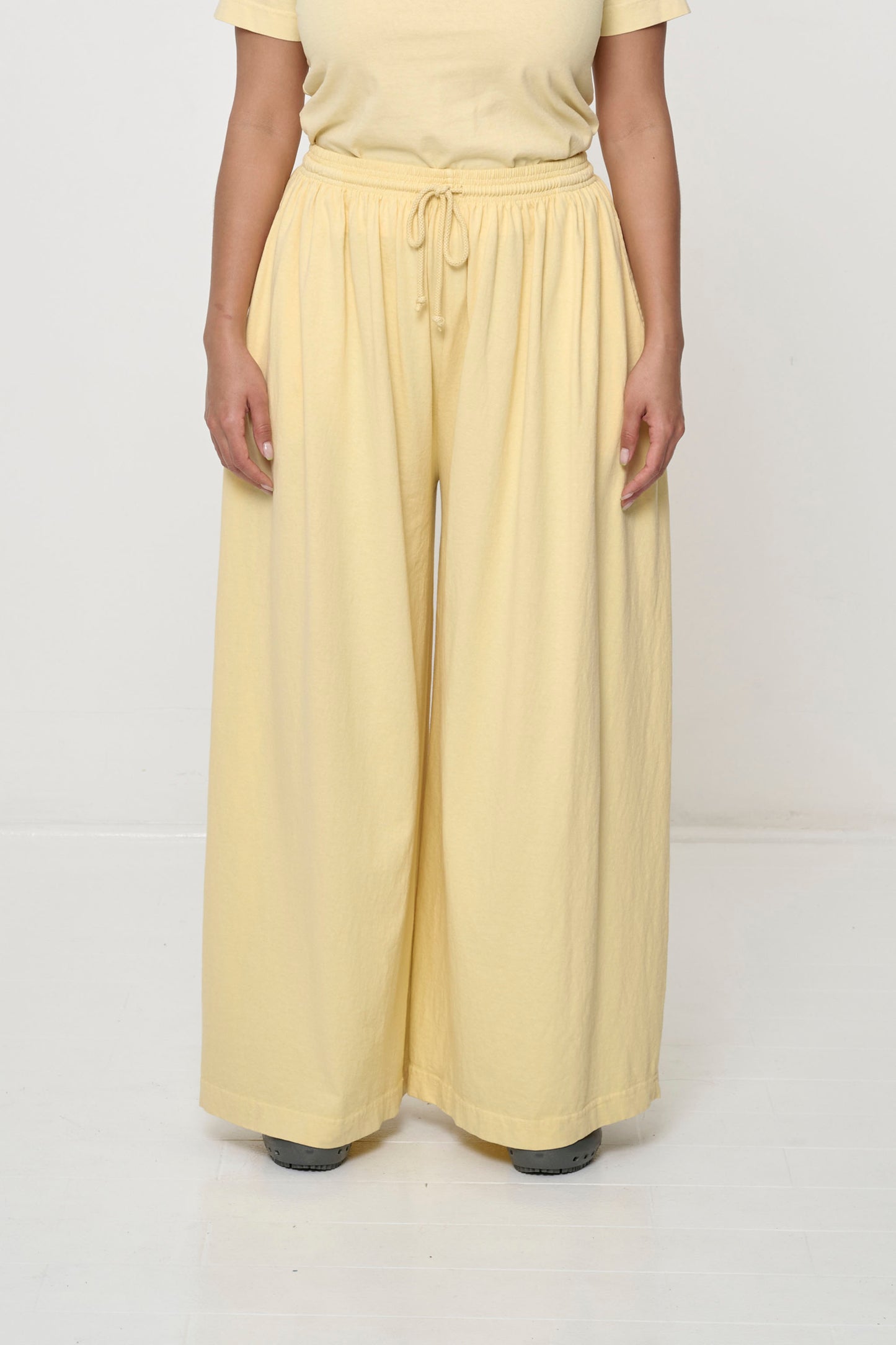 Front view: person in French Butter yellow Tubular Pants, featuring elastic waistband, drawcord, relaxed drape.