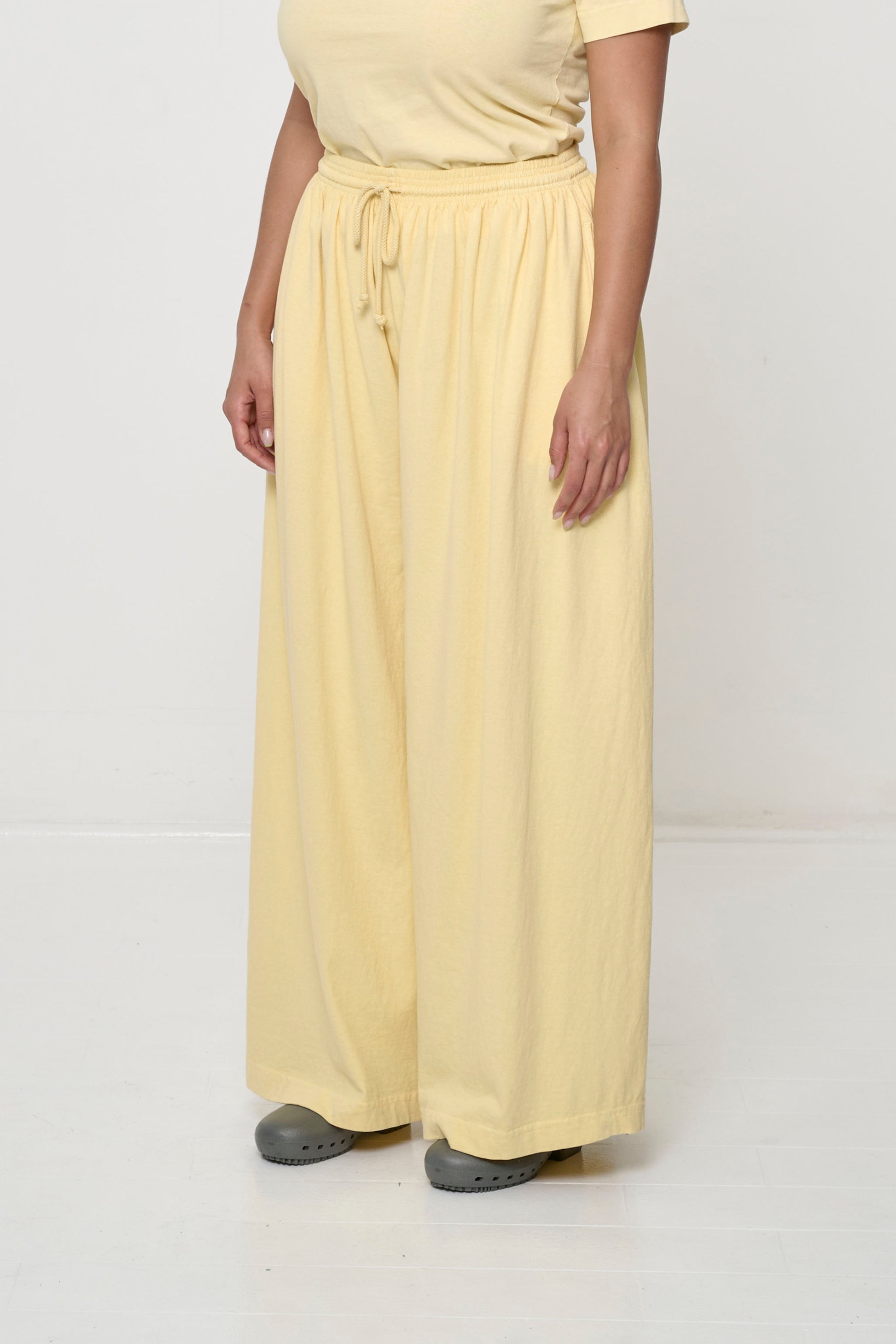 Person facing 45-degrees to the front in French Butter Tubular Pants, showing lack of side seams and flowing wide pant legs.