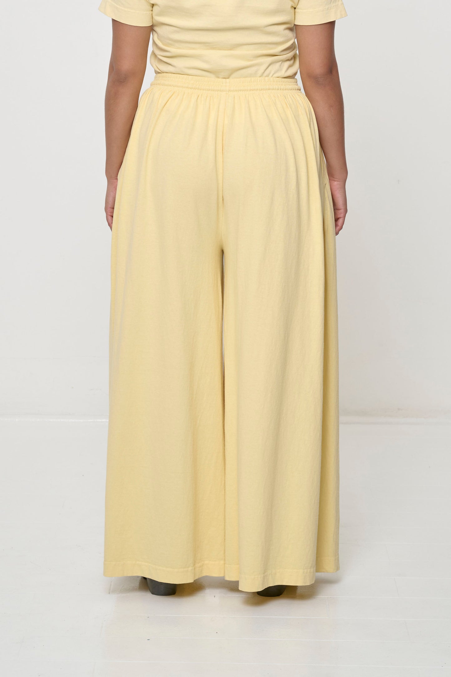 Back view: Lower 2/3 of a person wearing French Butter Tubular Pants, flowing vertical fabric folds.