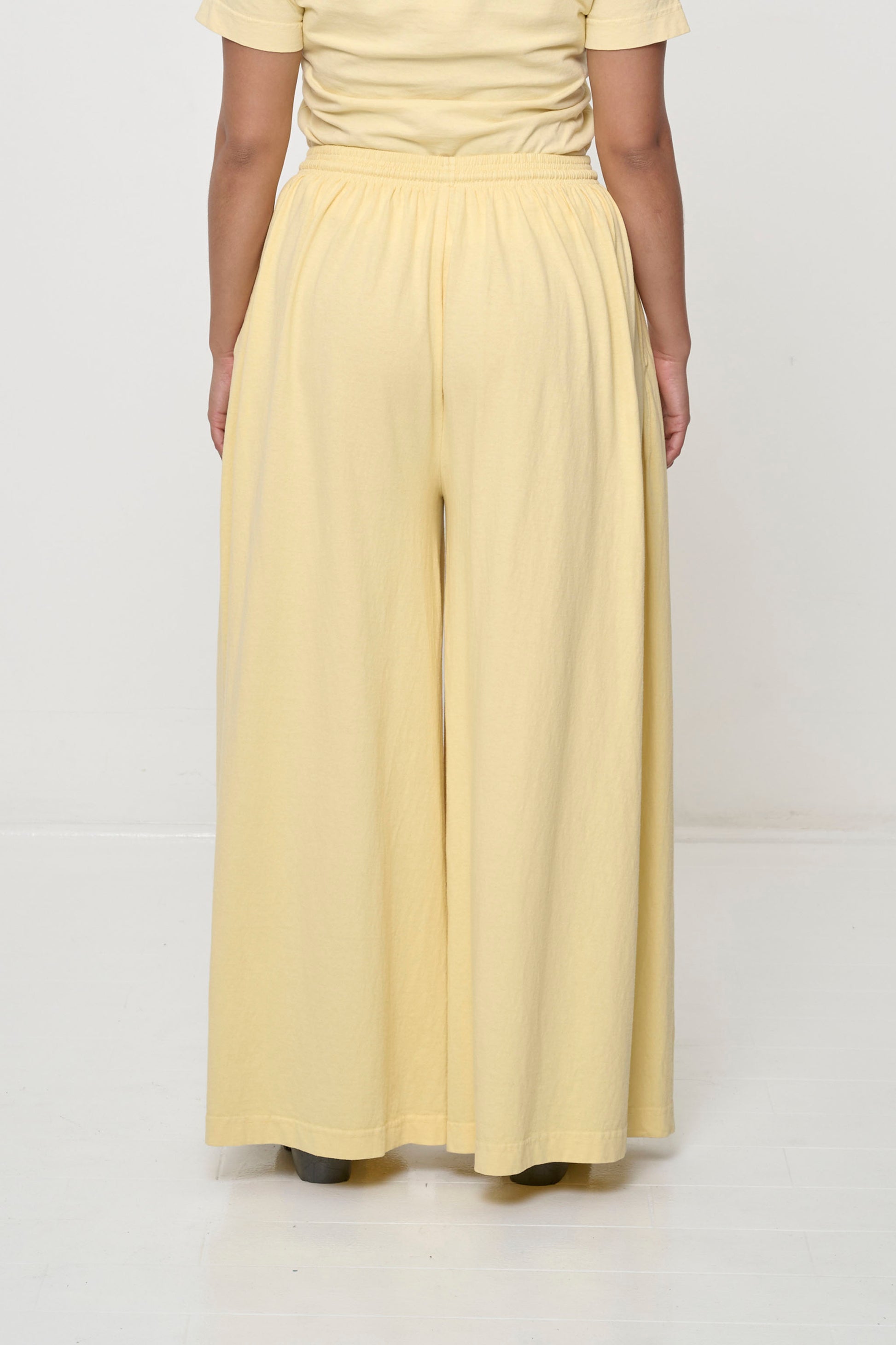 Back view: Lower 2/3 of a person wearing French Butter Tubular Pants, flowing vertical fabric folds.