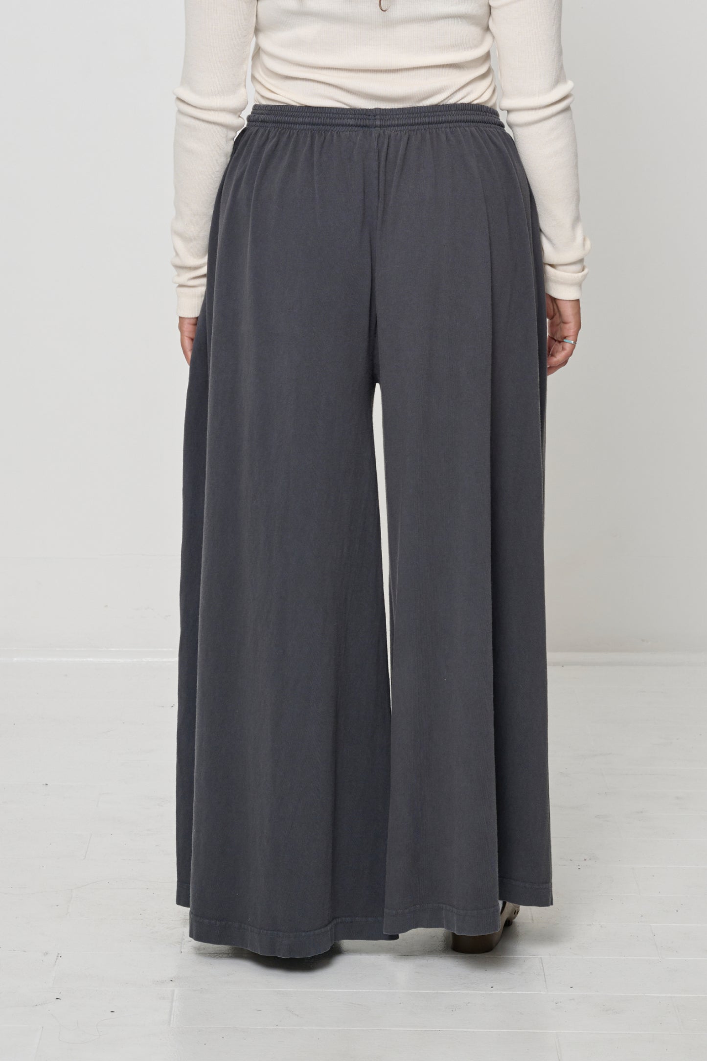 Back view: Lower 2/3 of a person wearing Slate Tubular Pants, flowing vertical fabric folds.