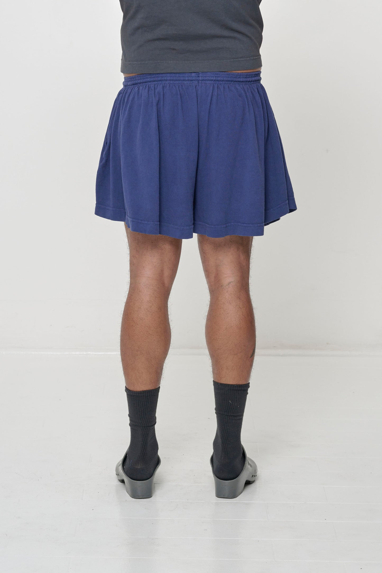 Back view: Lower 3/4 of a person wearing Washed Navy Tubular Shorts, flowing vertical fabric folds.