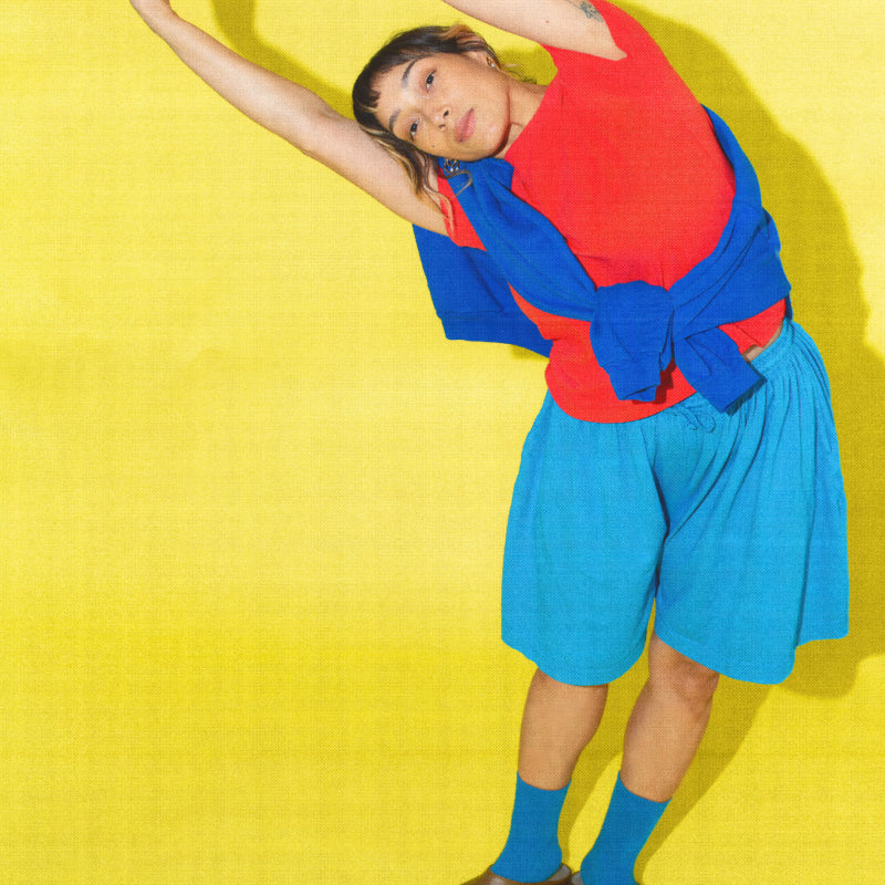 A woman wearing Apartment Pants sitting on the floor against a pink background