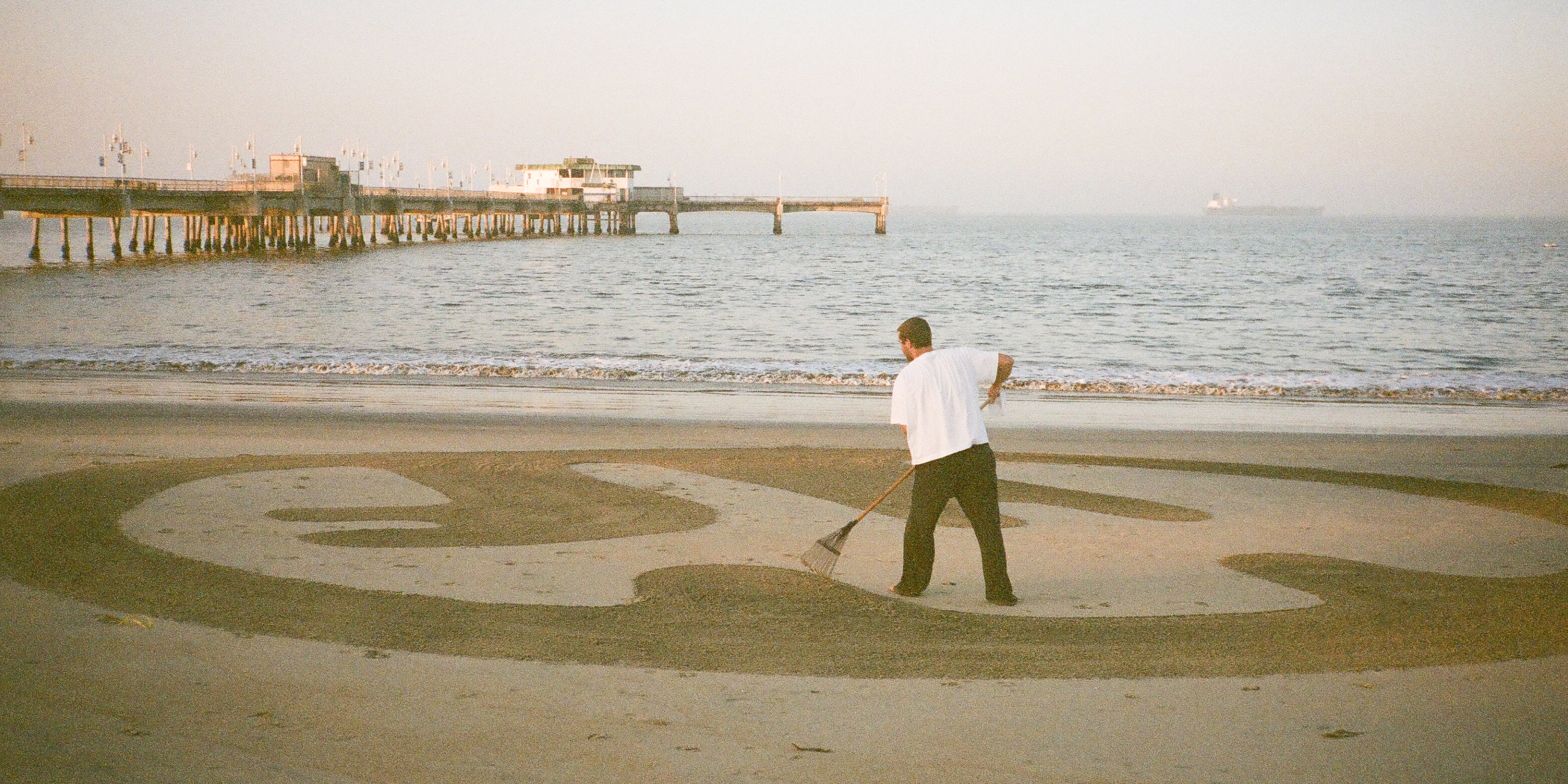 A man on the beach rakes the sand to show the Everybody.World logo