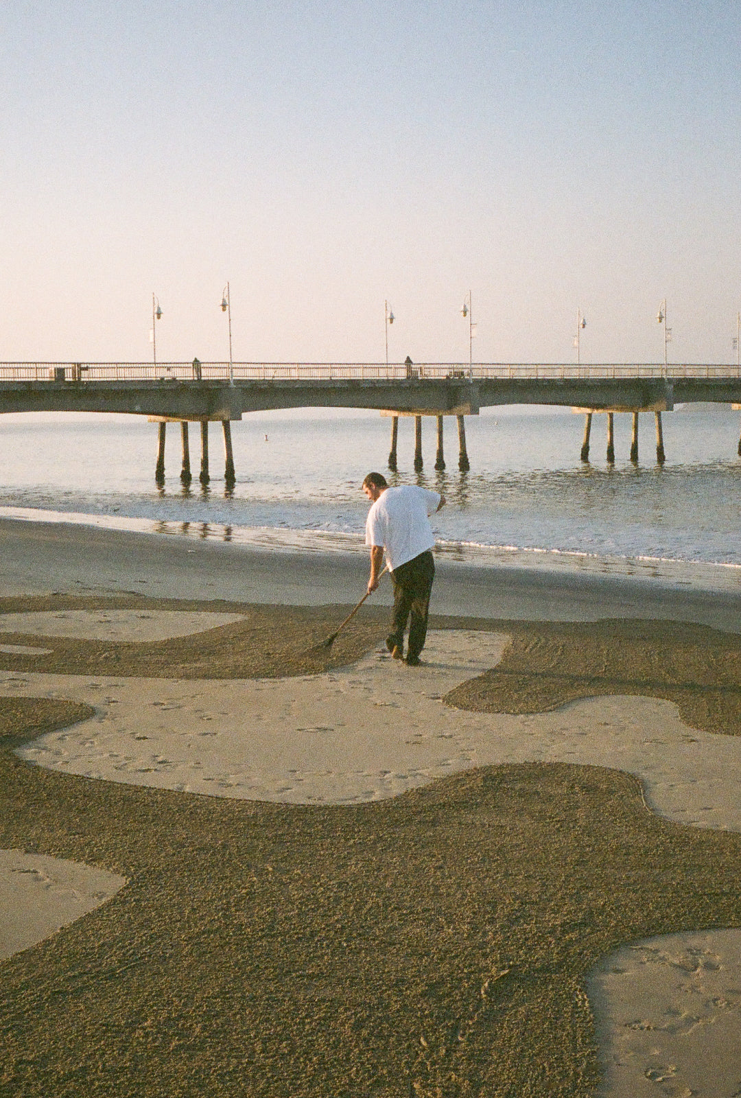 A man on the beach rakes the sand to show the Everybody.World logo