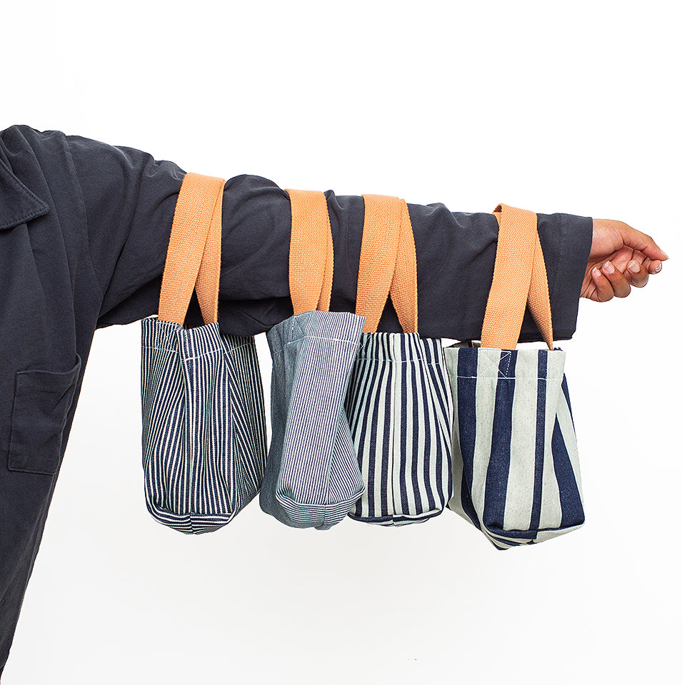 Four Scrap Totes held out on person's arm, wearing Ruby Trash Tee in Slate.