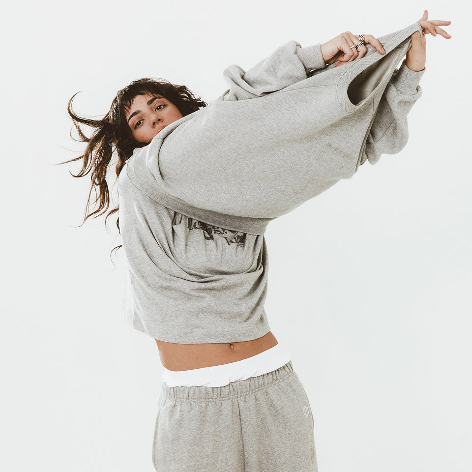 Woman wearing Heather Sweatpants and in the middle of putting on a Heather Crewneck.