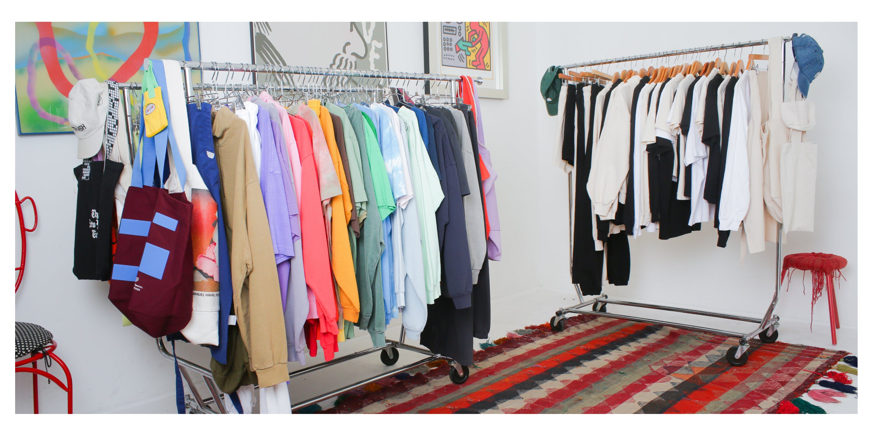 Clothing racks with custom merch and sustainable blanks in a room with art-adorned walls and a striped rug