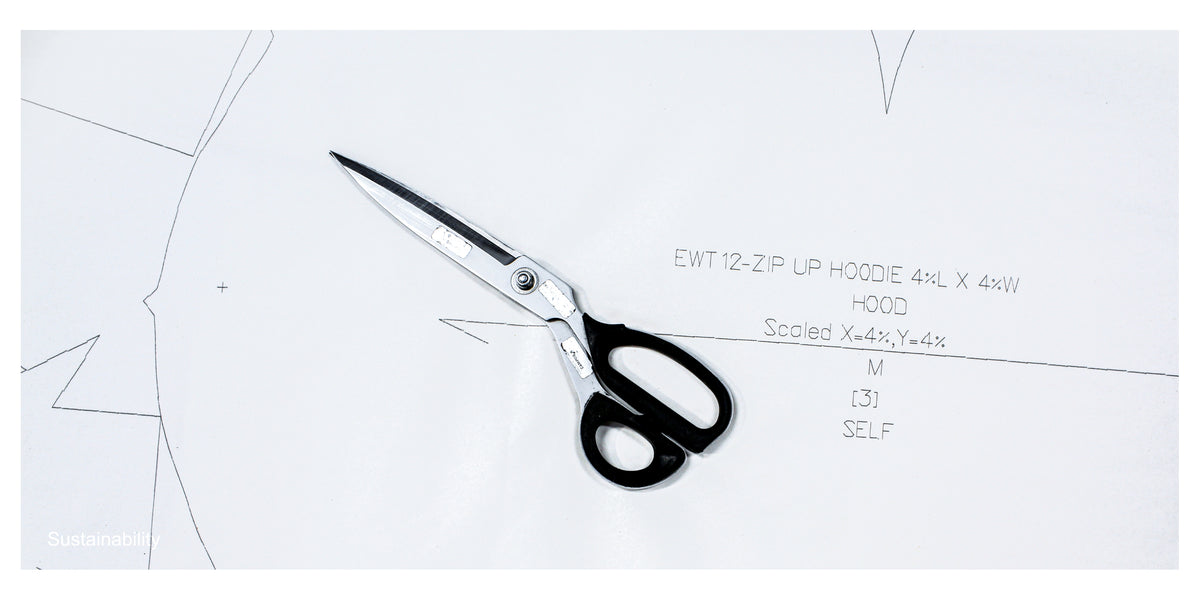 A pair of scissors with black handles and silver blades rests on a white sheet of paper with line art and handwritten text.