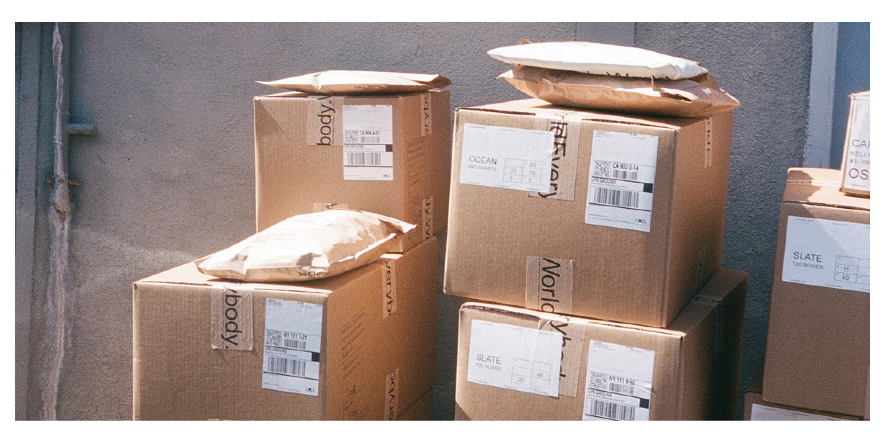 Stack of cardboard boxes with shipping labels and tape that reads 'Everybody.World' against a wall. 