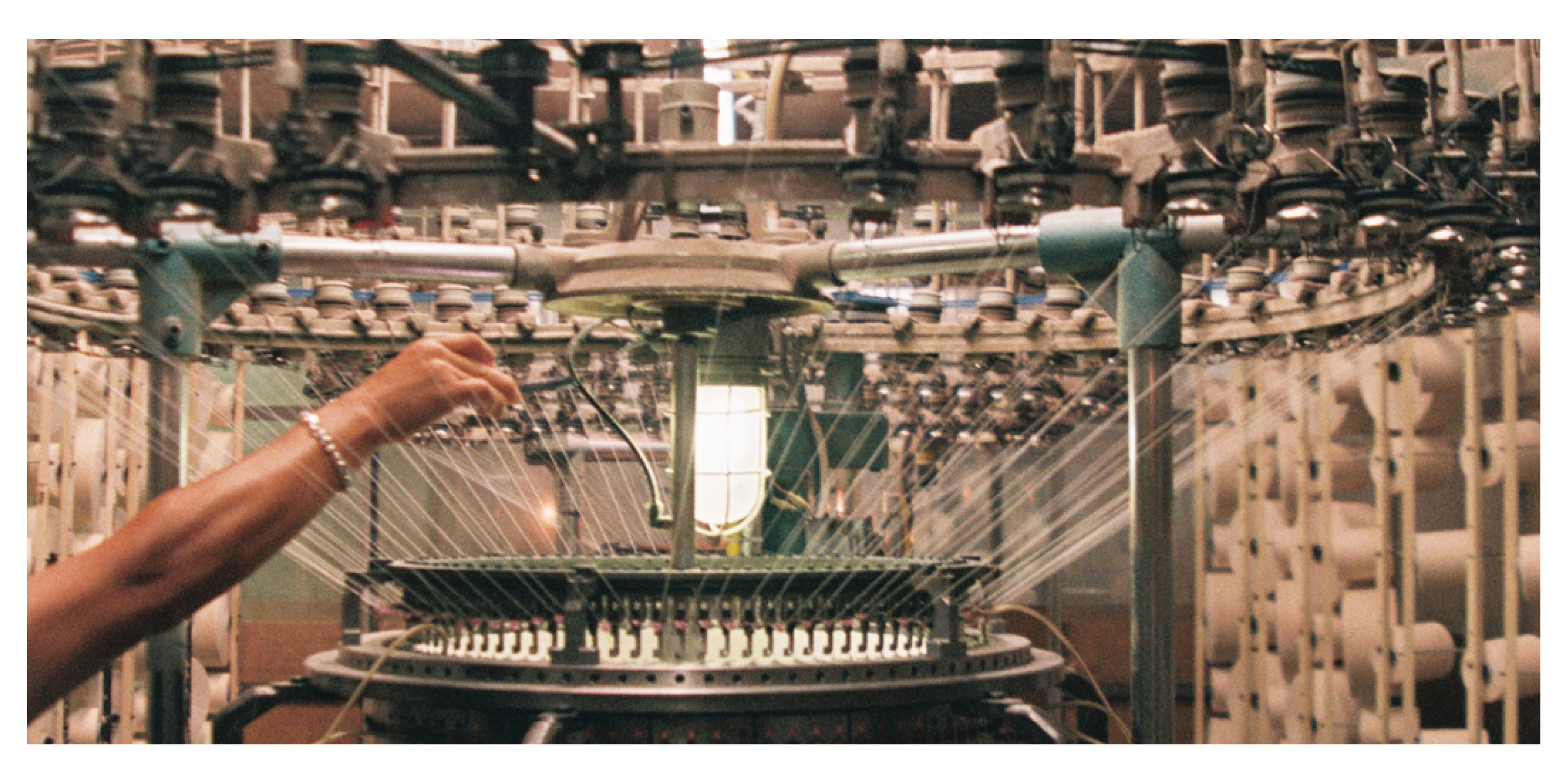 Person operating a knitting machine with intricate machinery in the background