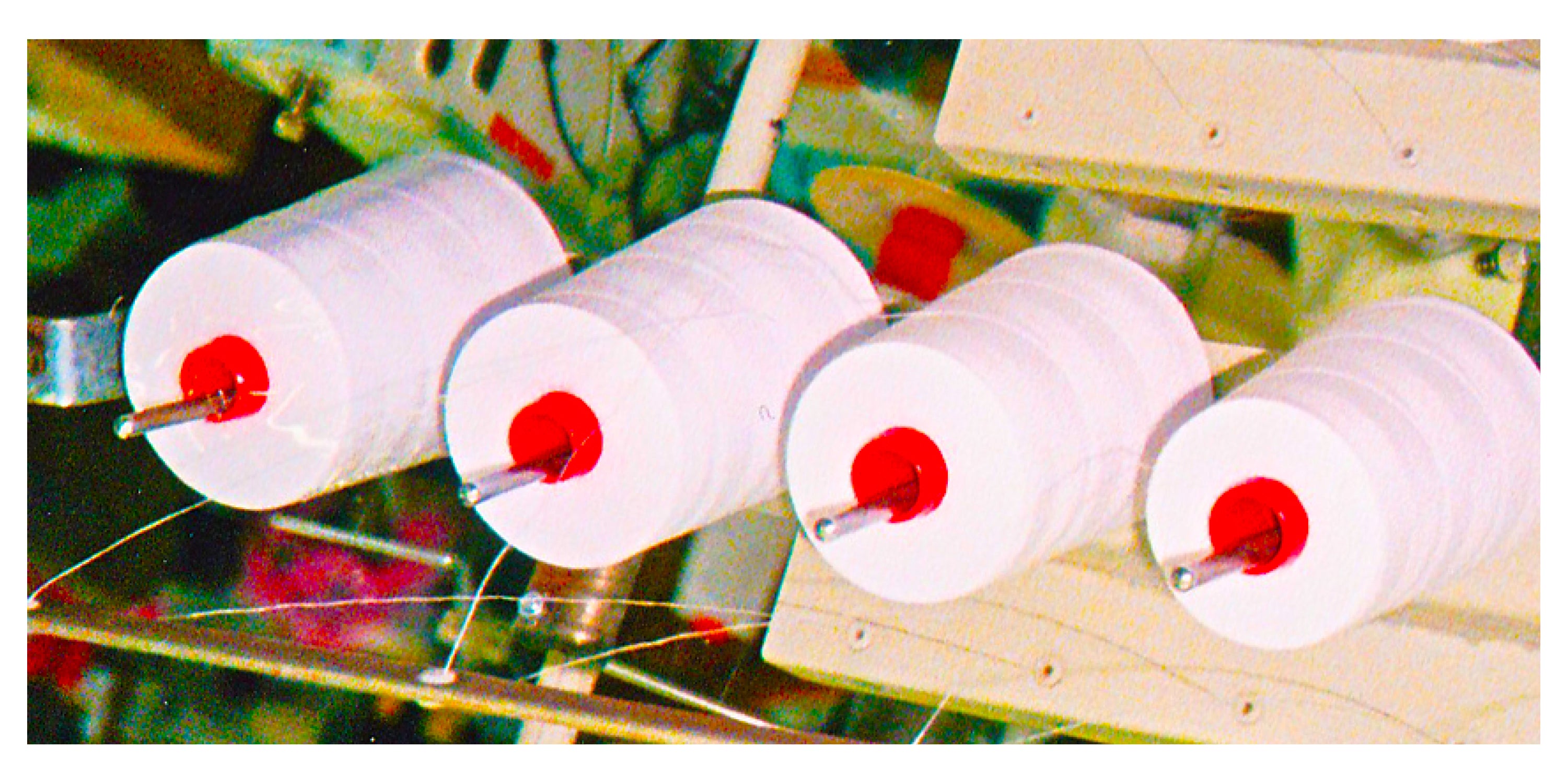 Four white cotton spools with red centers on a wooden stand.