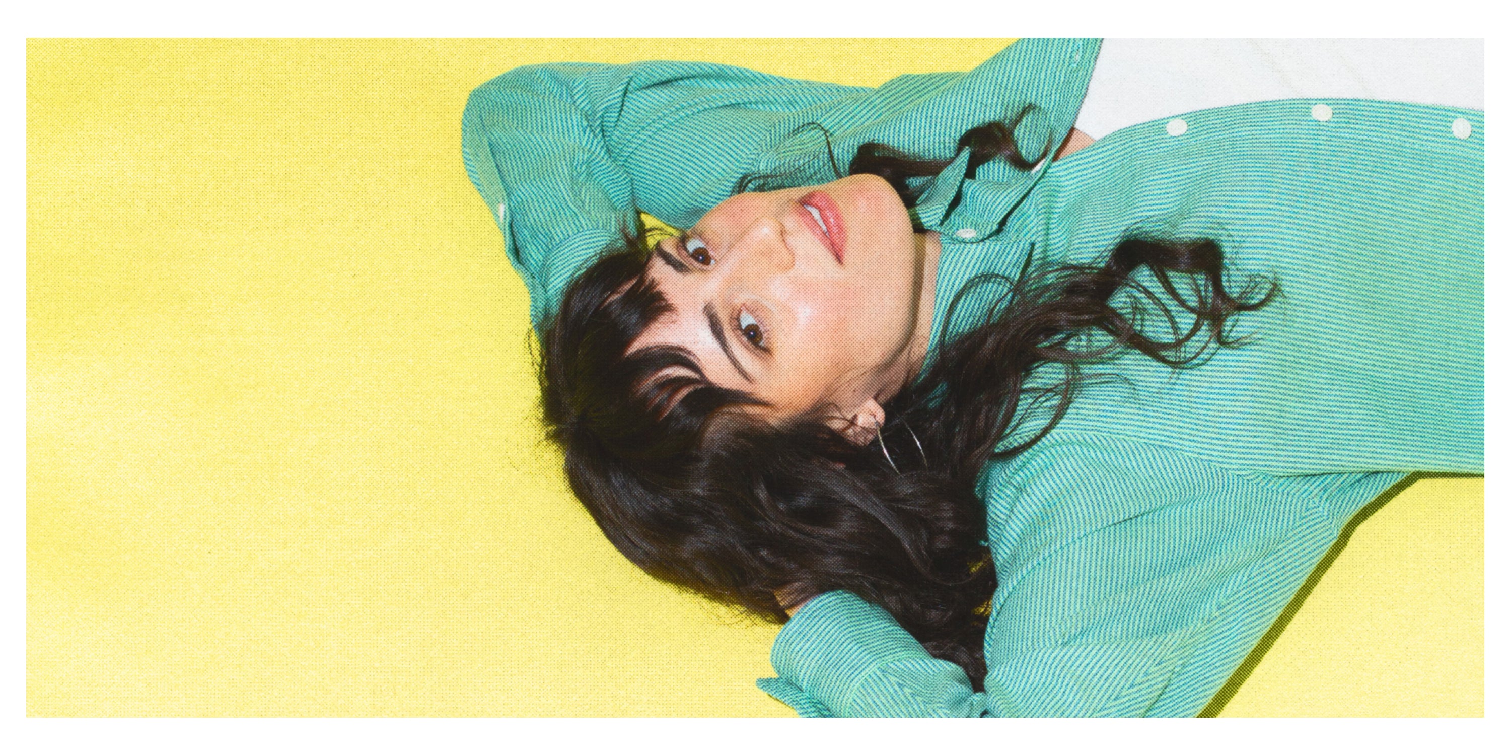 A woman lying down against a yellow backdrop with her hands behind her head