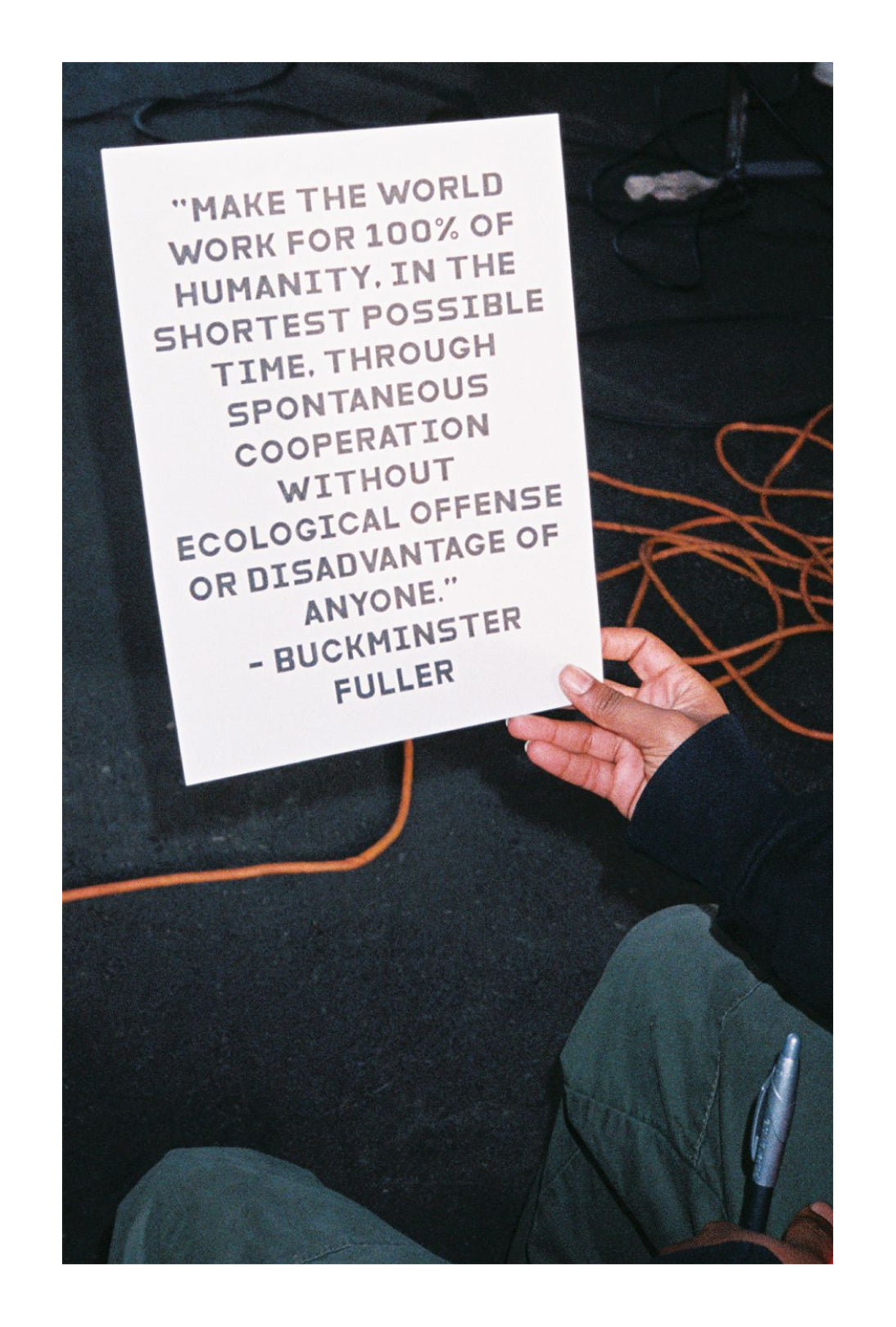 Person holding a sign with a quote by Buckminster Fuller against a dark background