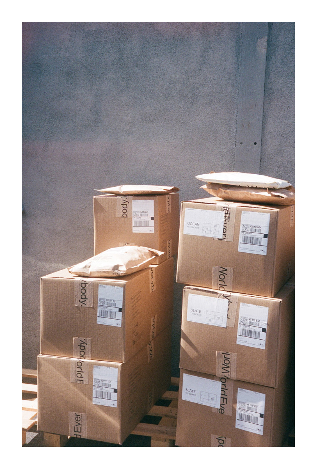 Stack of cardboard boxes with shipping labels and tape that reads 'Everybody.World' against a wall. 