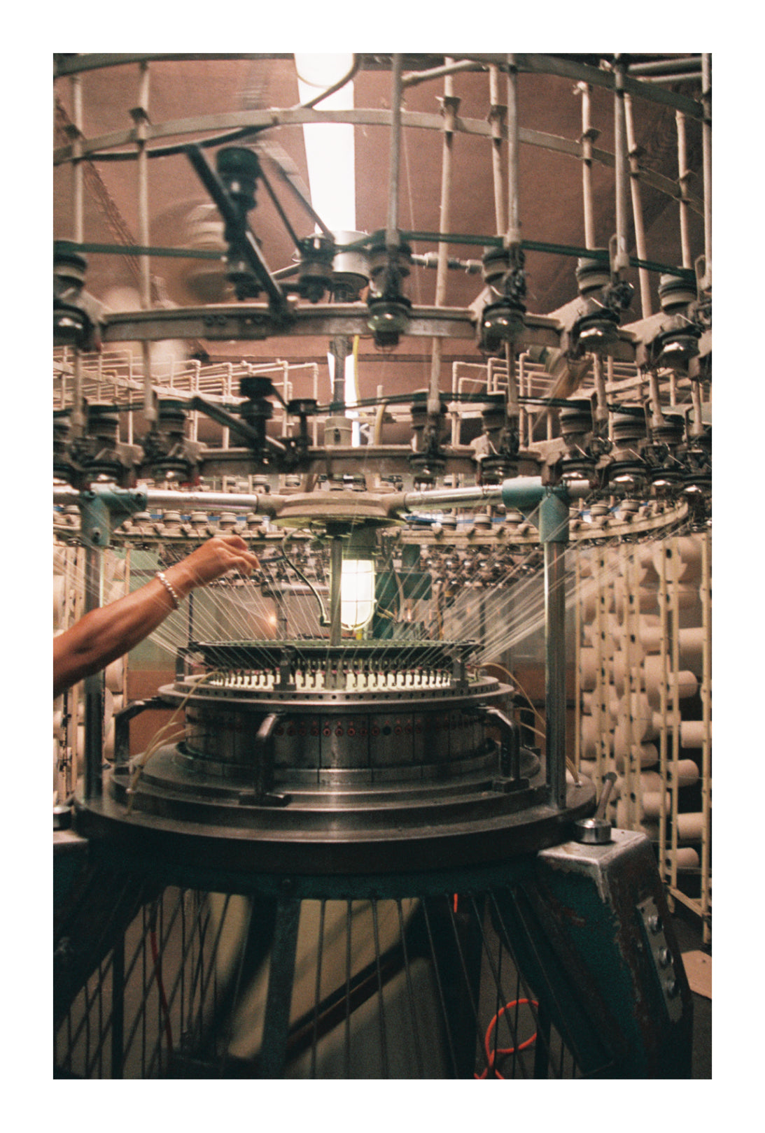 Person operating a knitting machine with intricate machinery in the background