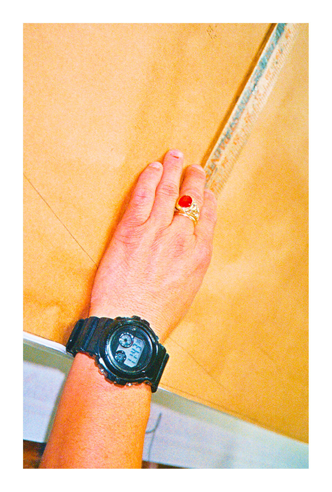 Hand wearing a black watch and red stone ring on a yellow background