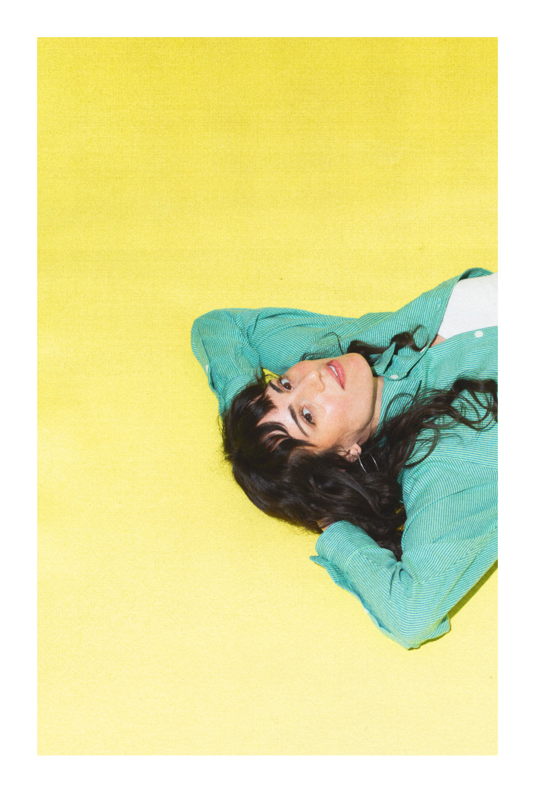 A woman lying down against a yellow backdrop with her hands behind her head