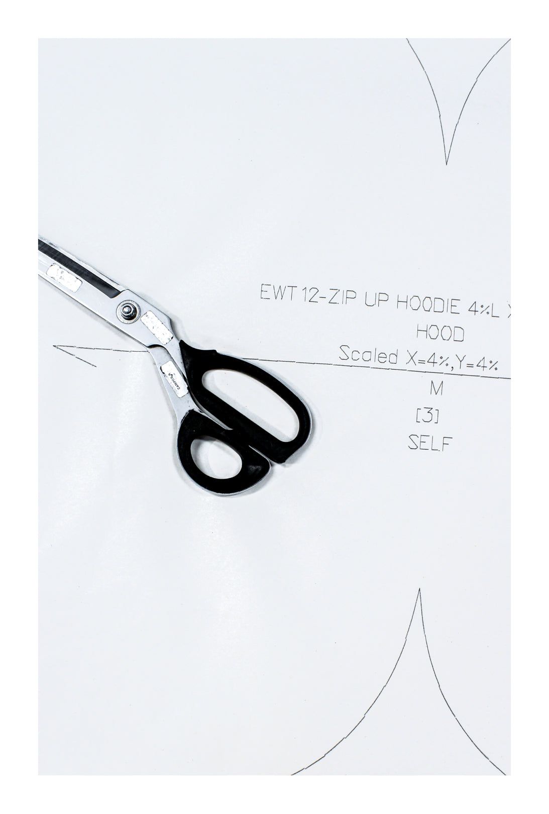 A pair of scissors with black handles and silver blades rests on a white sheet of paper with line art and handwritten text.