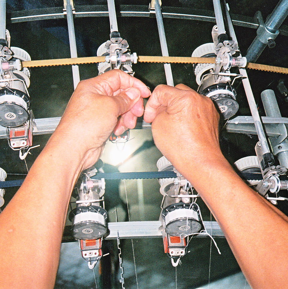 Hands operating a machine with multiple spools of thread.