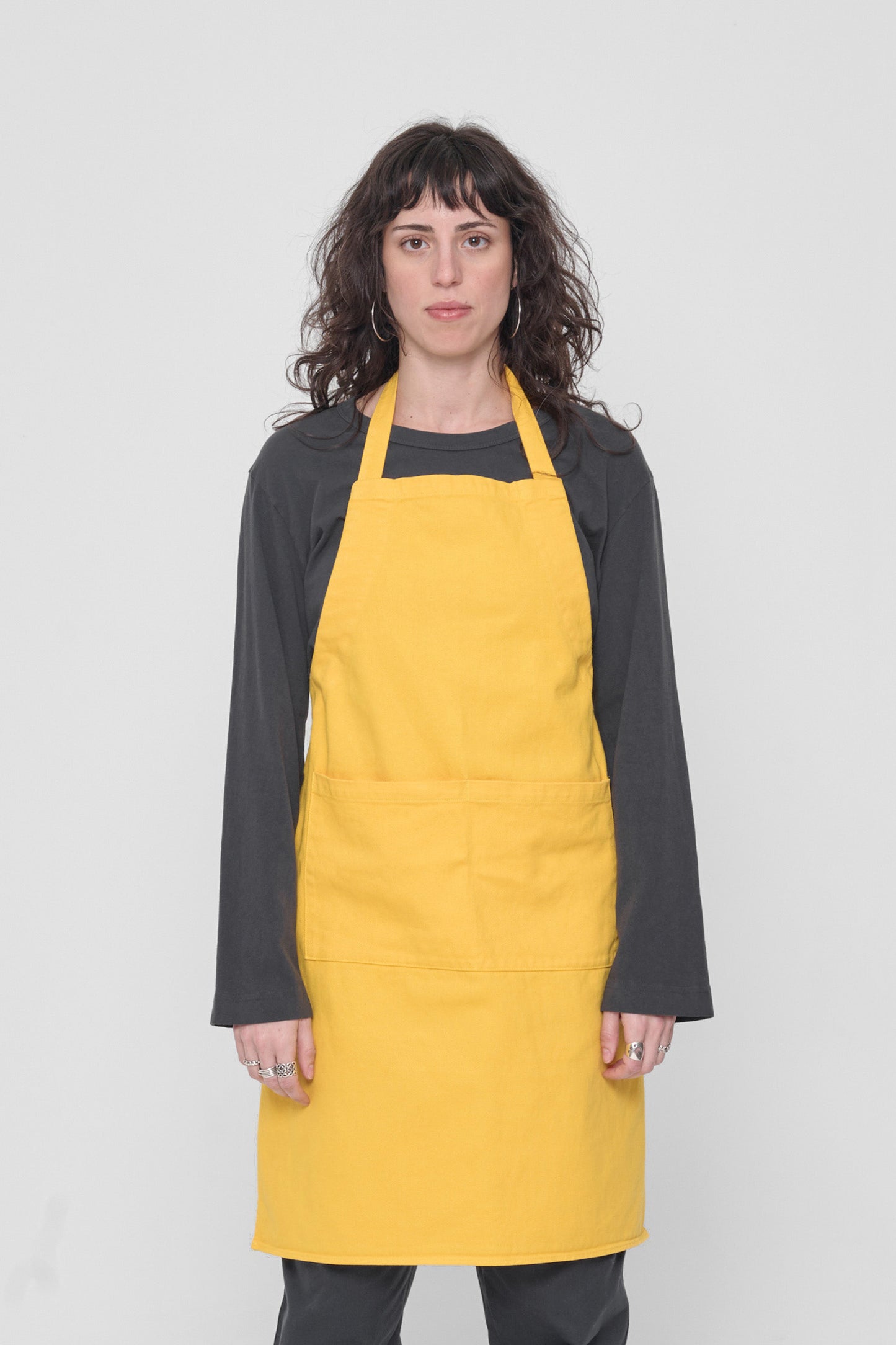 Front view: a person in an Everybody Yellow Adjustable Apron. Straps tied behind their back.
