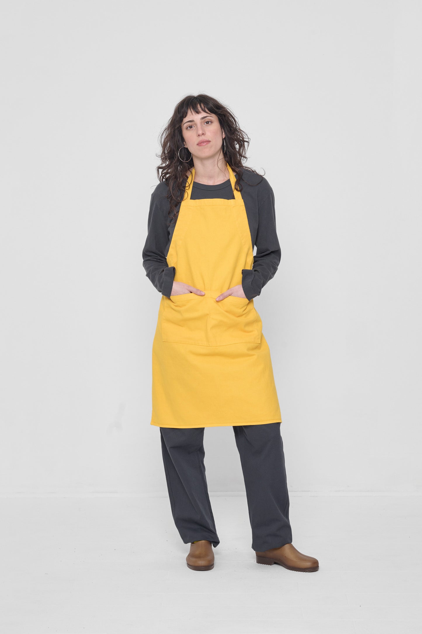 Apron covers the the woman's chest to knees. Her hands are in the large front pocket.