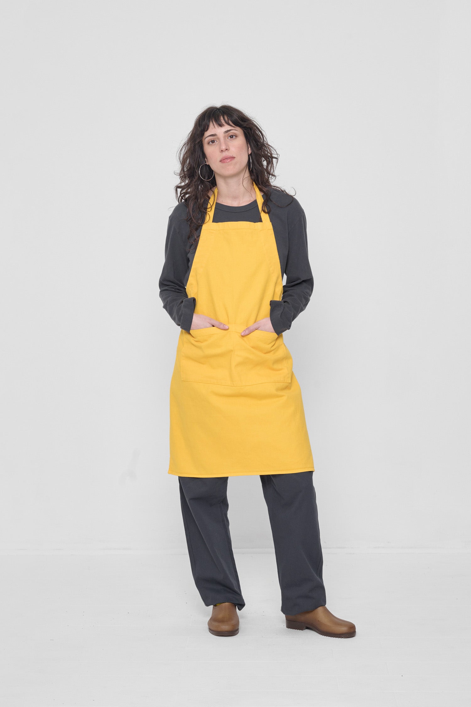 Apron covers the the woman's chest to knees. Her hands are in the large front pocket.