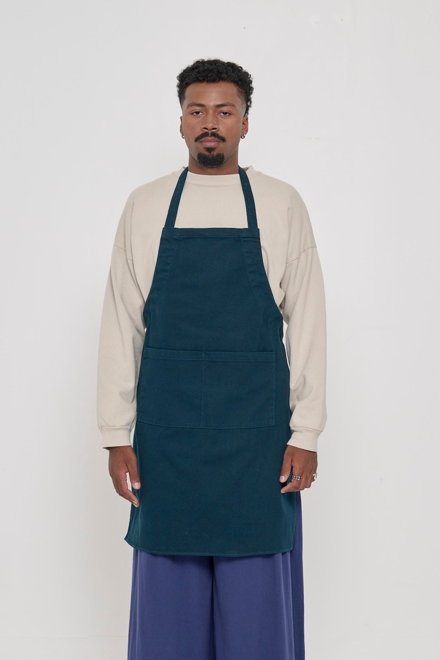 Front view of a person in an Adjustable Apron in Juniper, with straps tied behind their back.