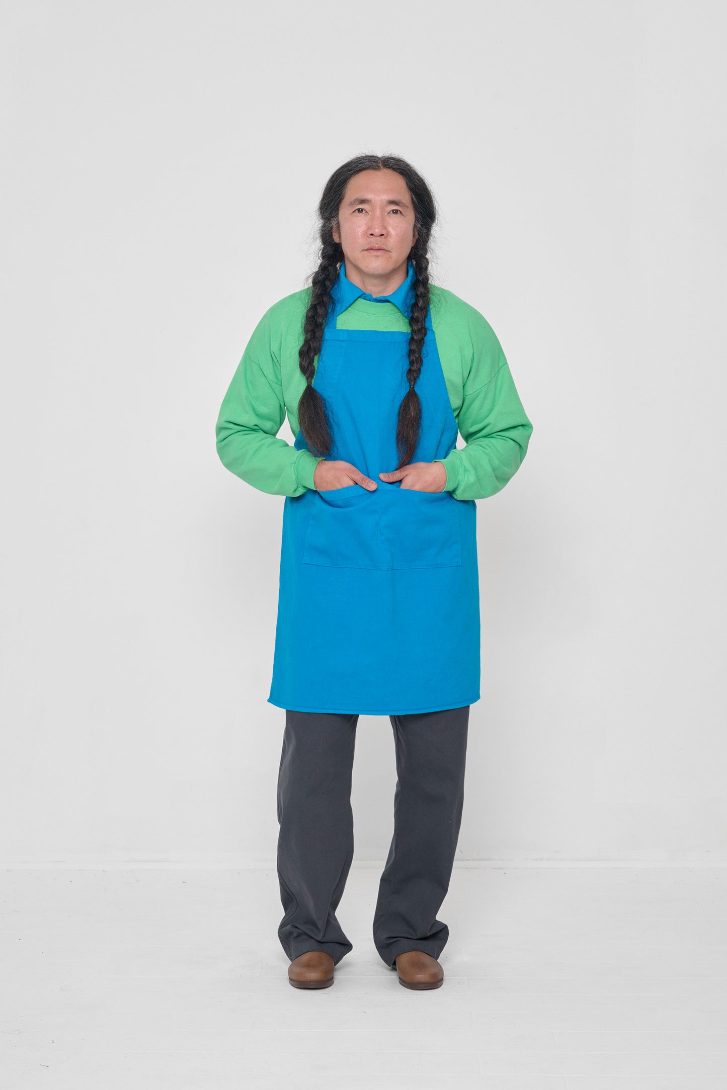 Apron covers the man's chest to knees. He has both hands in large front pocket.