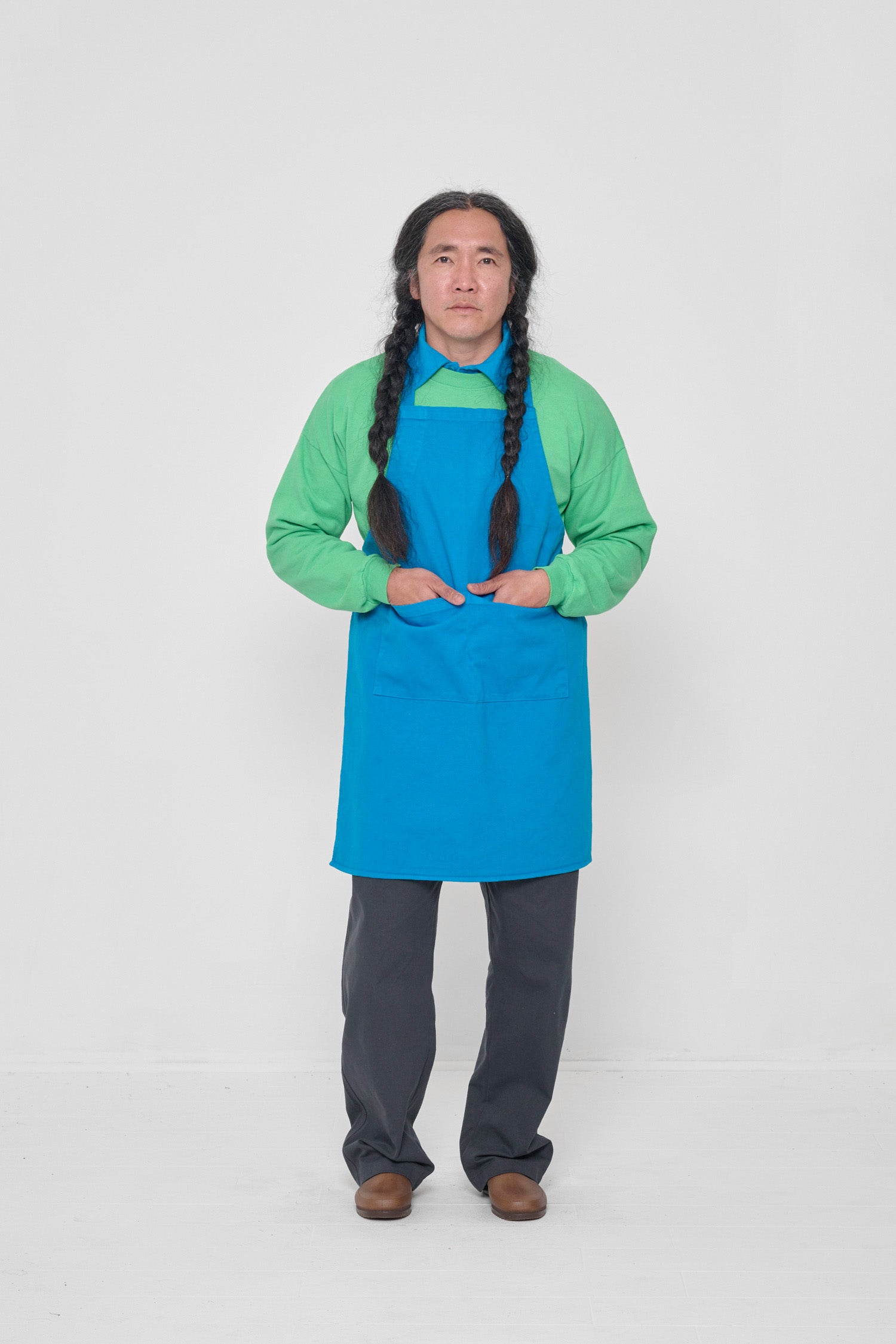 Apron covers the man's chest to knees. He has both hands in large front pocket.