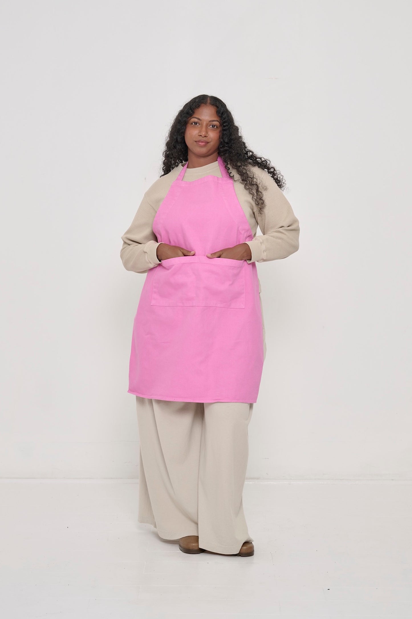 Pixie Adjustable Apron on a woman, covering chest to knees, hands in large front pocket.