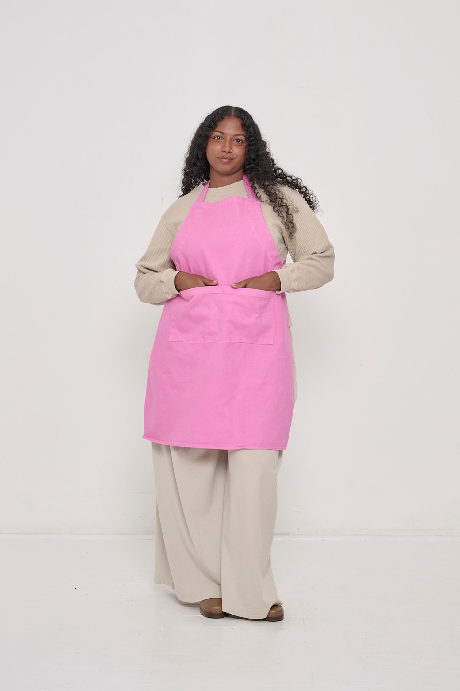 Pixie Adjustable Apron on a woman, covering chest to knees, hands in large front pocket.
