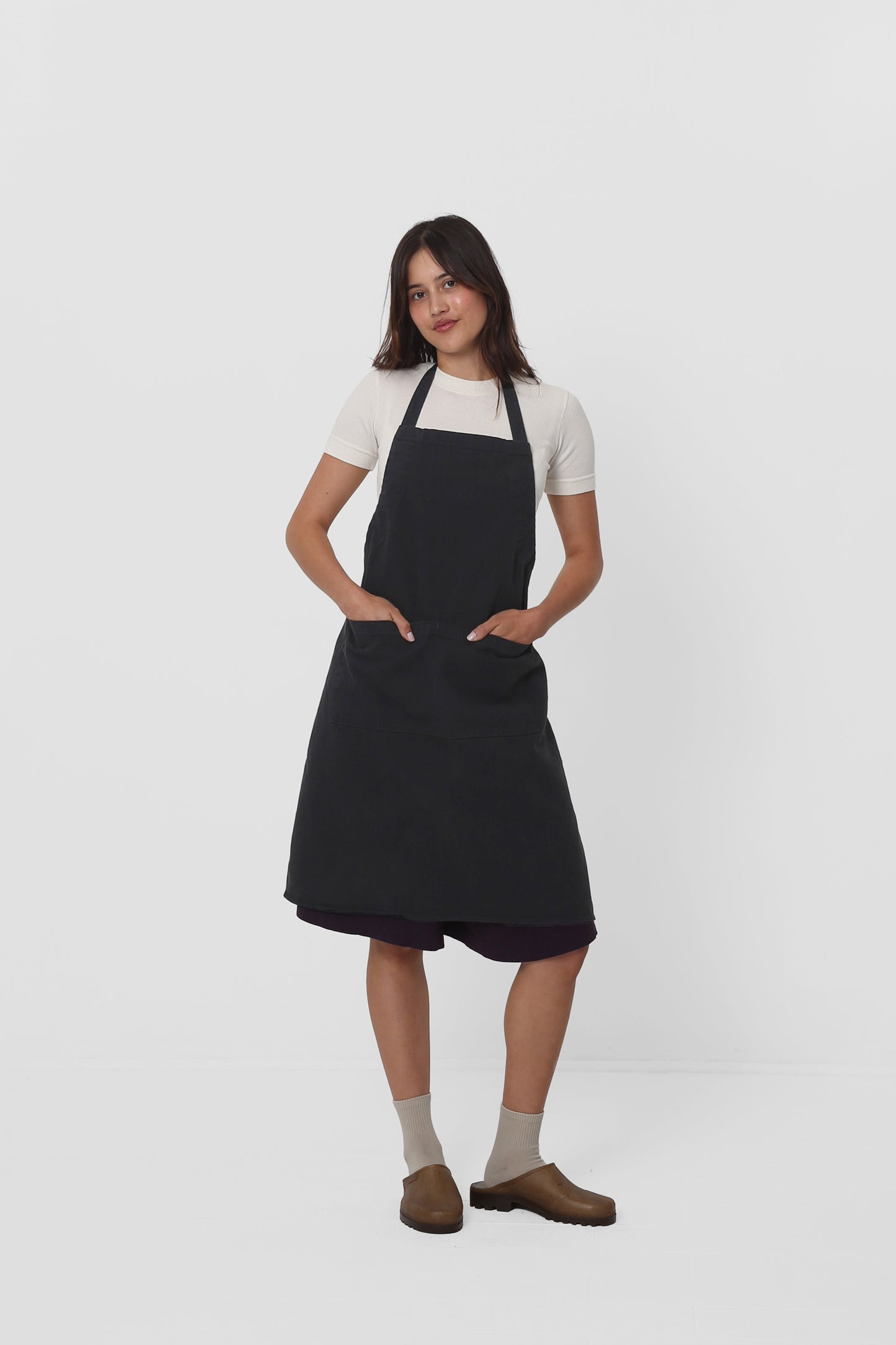 Apron covers the woman's chest to knees. She has both hands in large front pocket.