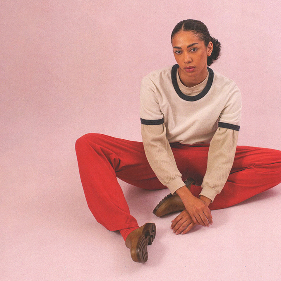 Woman sitting on the ground wearing Apartment Pants in Cedar, and a Ringer Trash Tee over the Thermal Boxier Long Sleeve Tee.