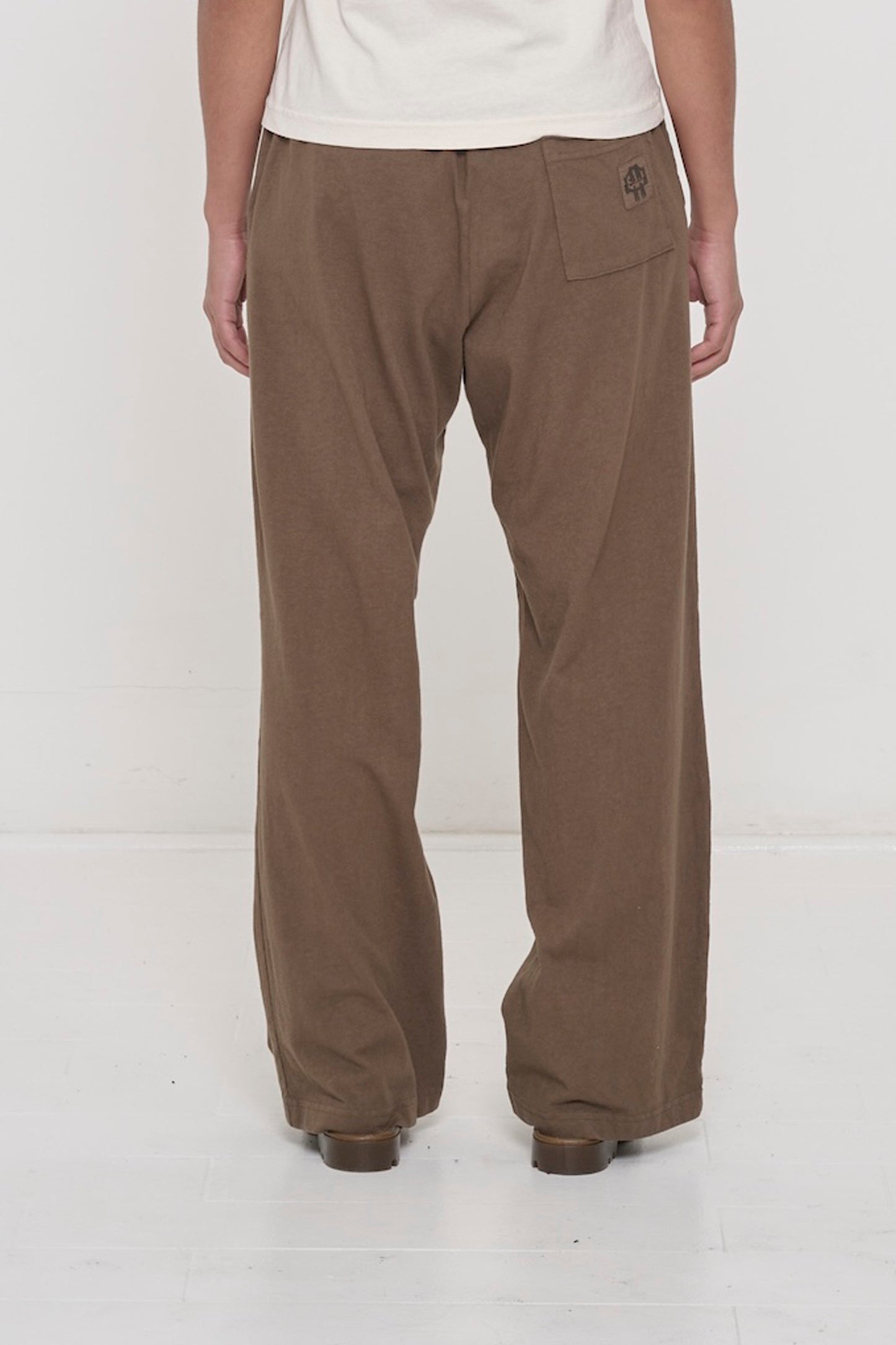 
Close-up back view of a person wearing Jerico's Apartment Pants in Dry Soil, showing the E.W logo printed on the back pocket.