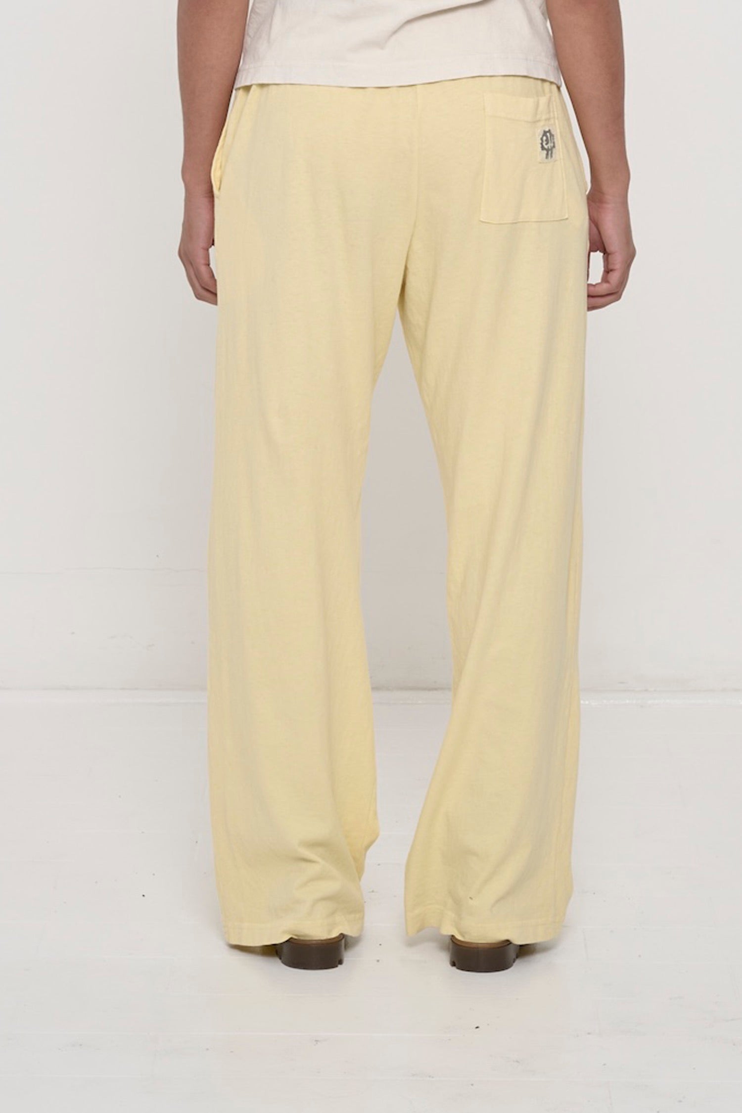 Back view, waist down: a person in French Butter Apartment Pants, highlighting the E.W logo printed on the back pocket.